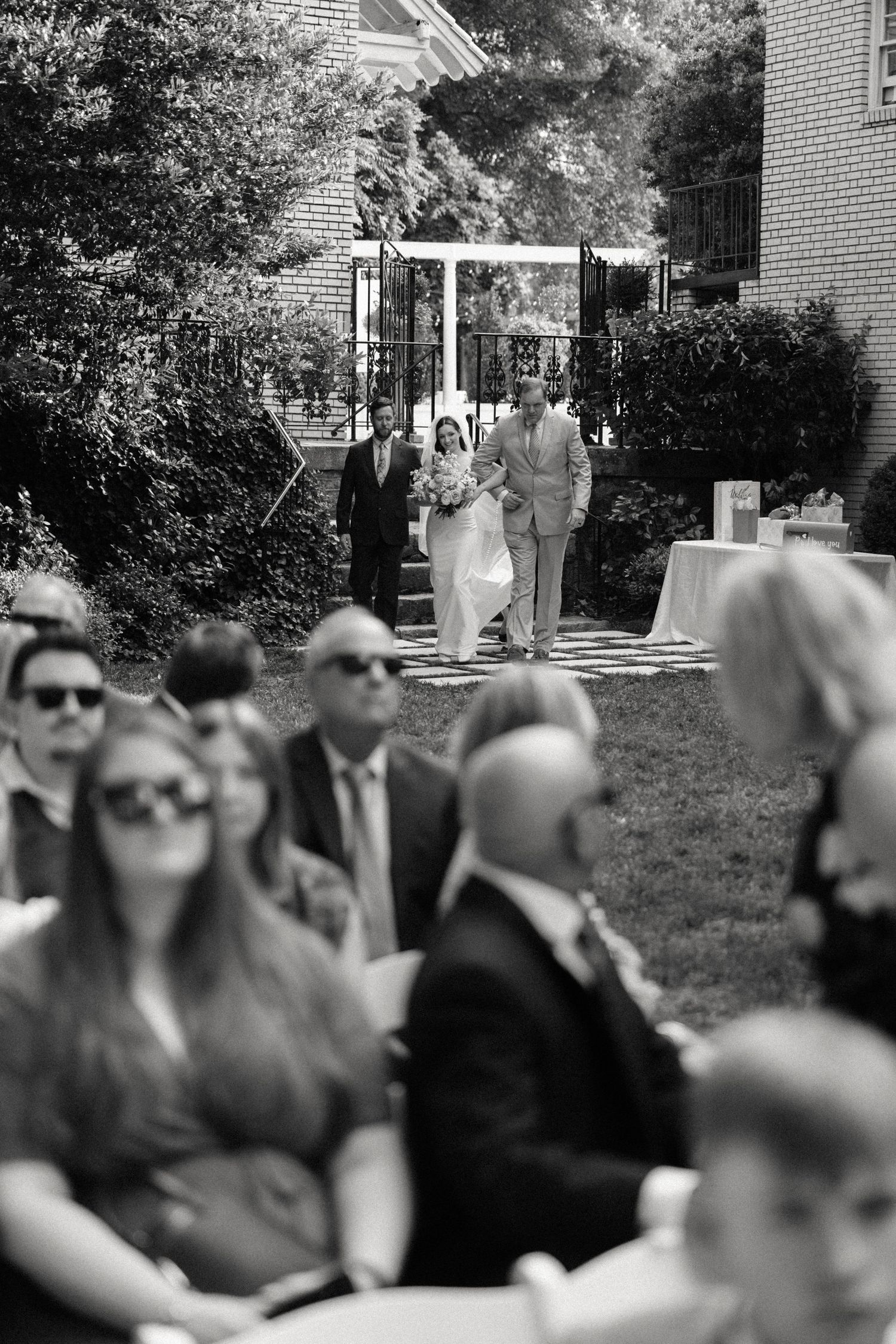 Black and white photo of wedding guests seated outdoors at a ceremony.