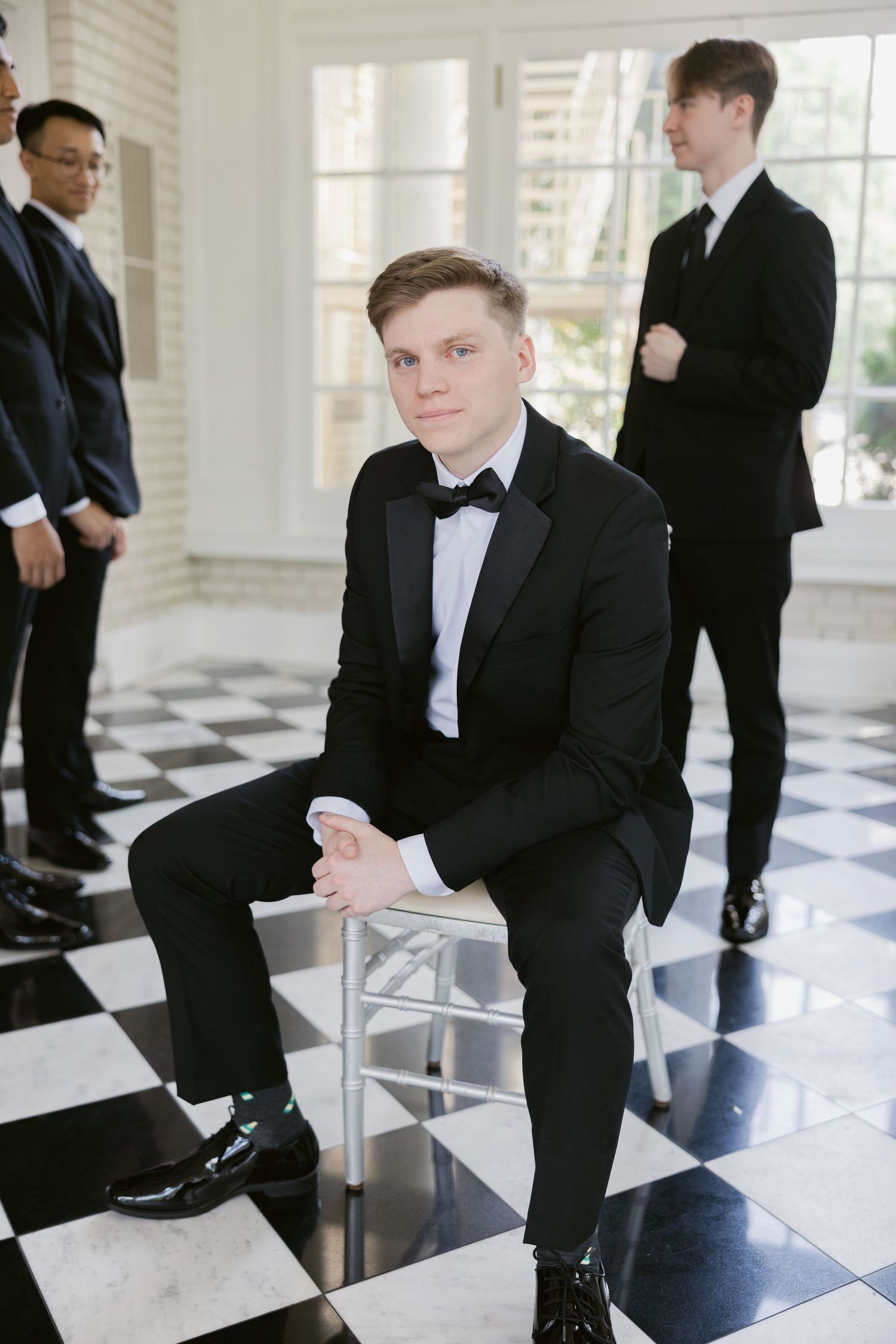 Groomsmen in black tuxedos posing on a black and white checkered floor.