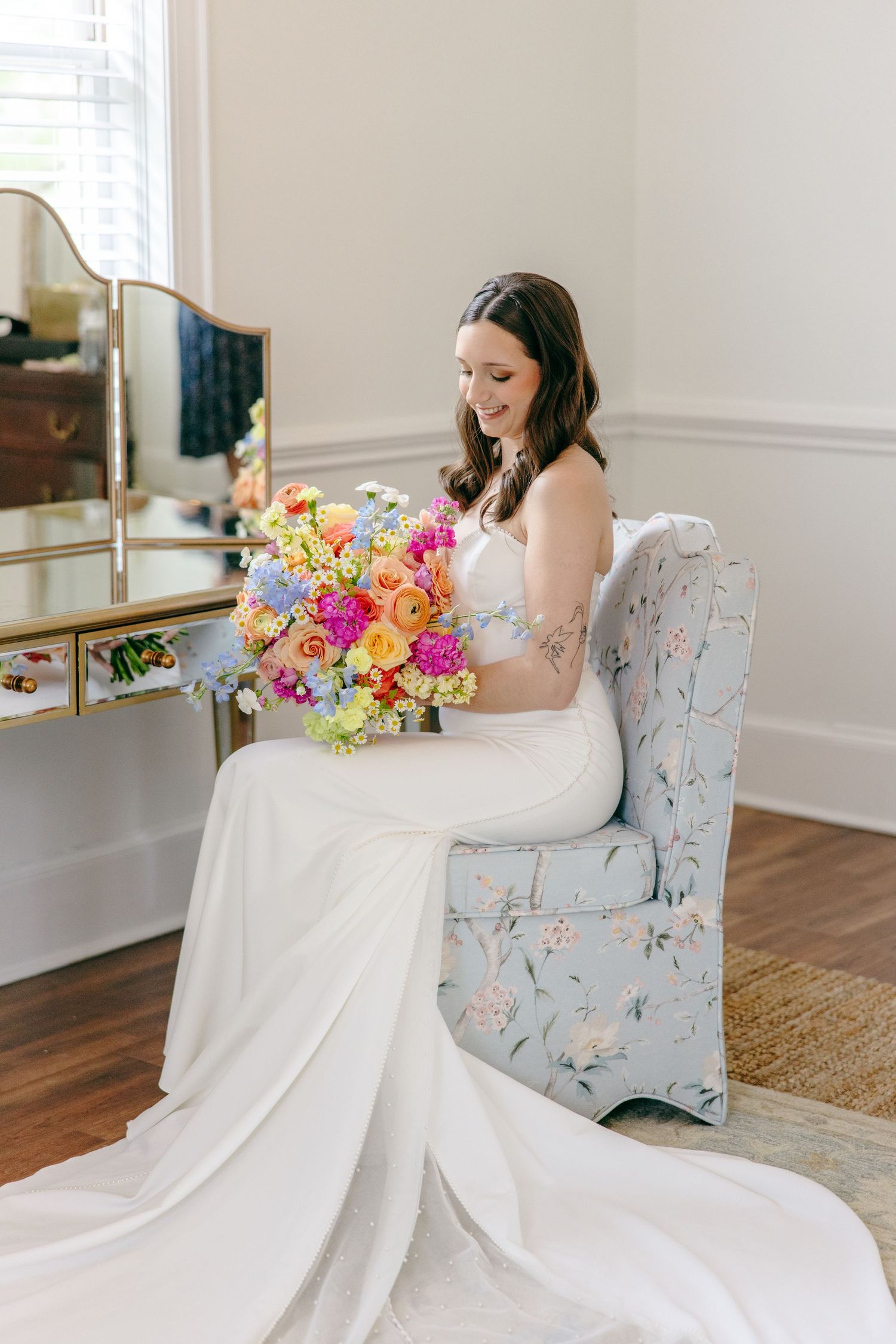 An elegant bridal portrait featuring a white wedding dress, floral chair, and colorful spring bouquet.