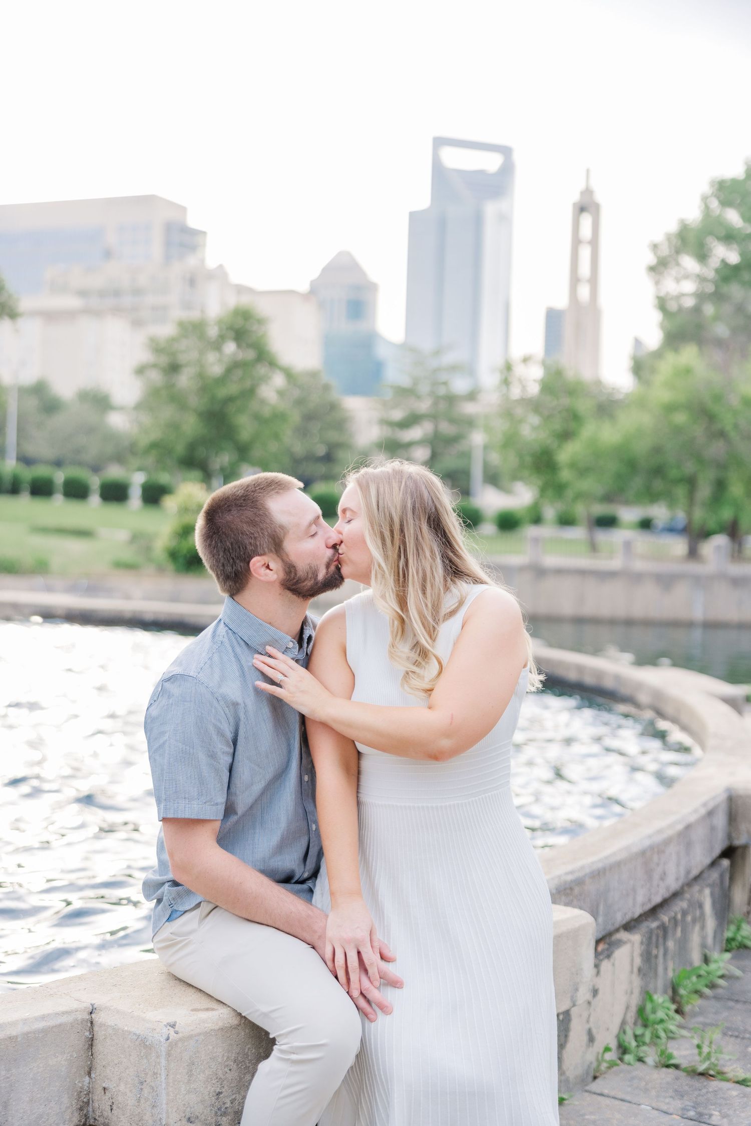 Romantic couple shares tender moments along a waterfront promenade with city buildings in the background.