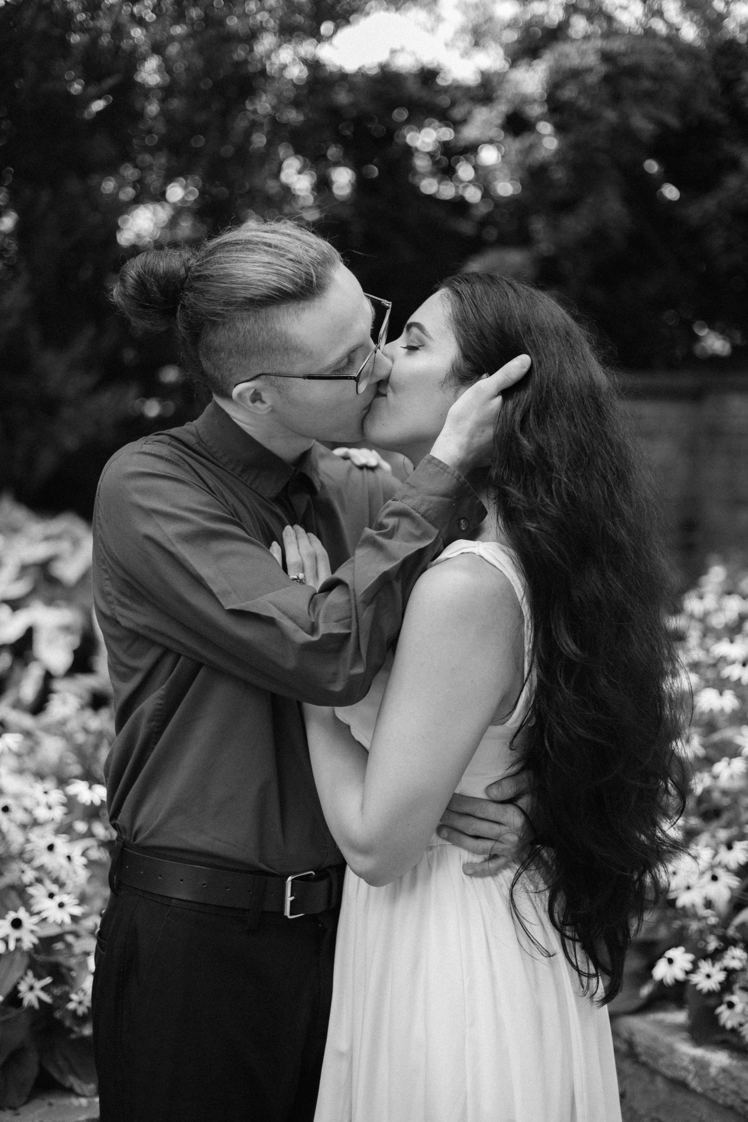 A romantic black and white photo series showing a couple sharing intimate kisses in a garden setting.