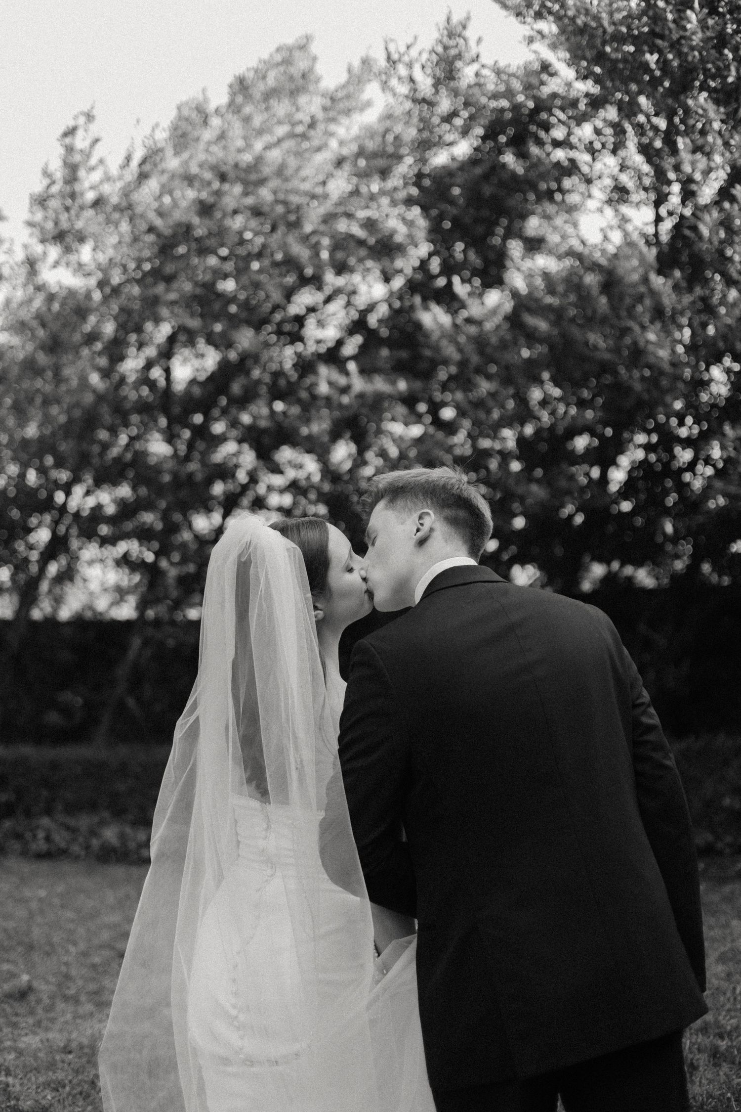 Black and white photo of bride and groom sharing intimate moment in outdoor garden setting.