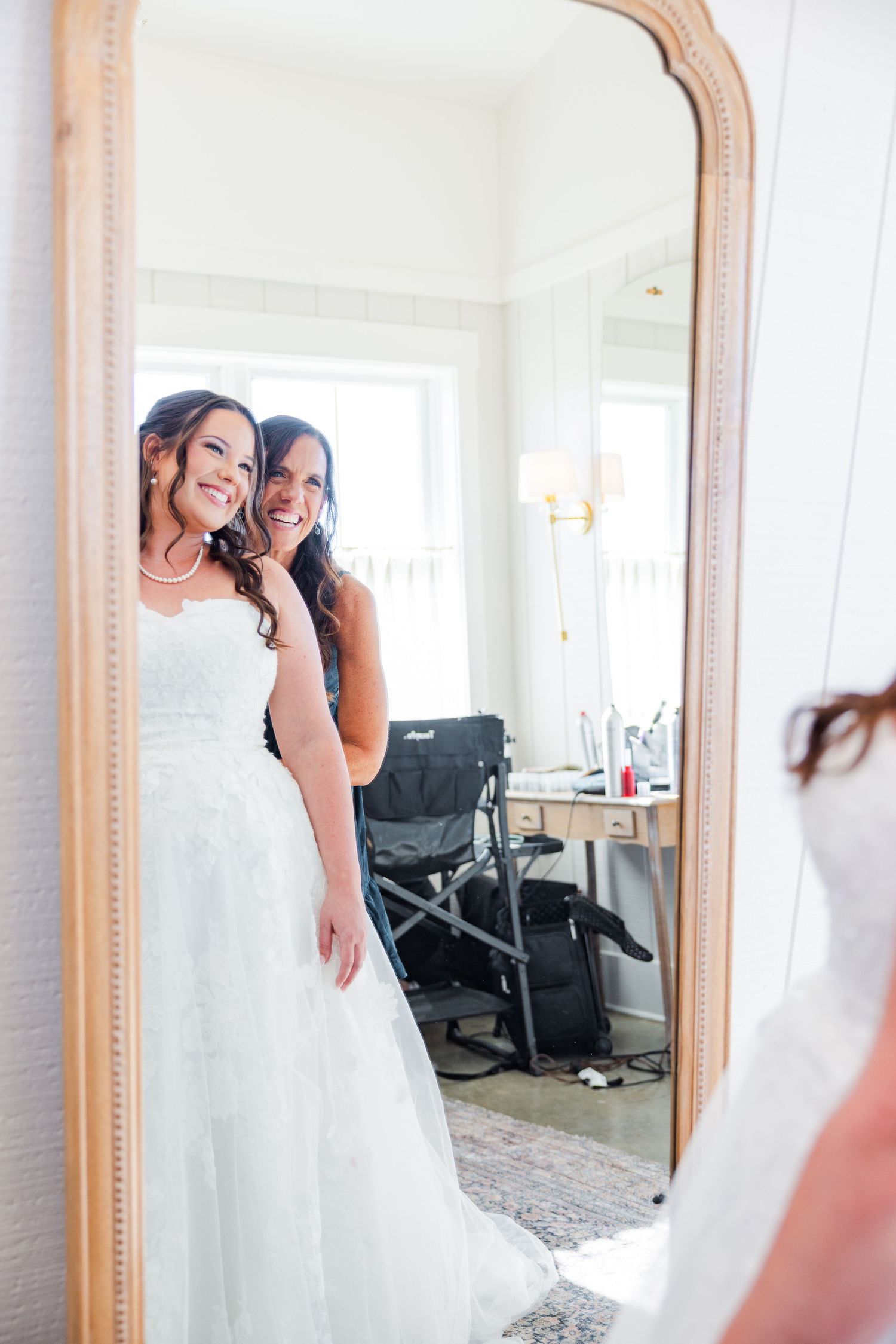 Bride and bridesmaids sharing joyful moments while getting ready in a bright, mirror-filled dressing room.