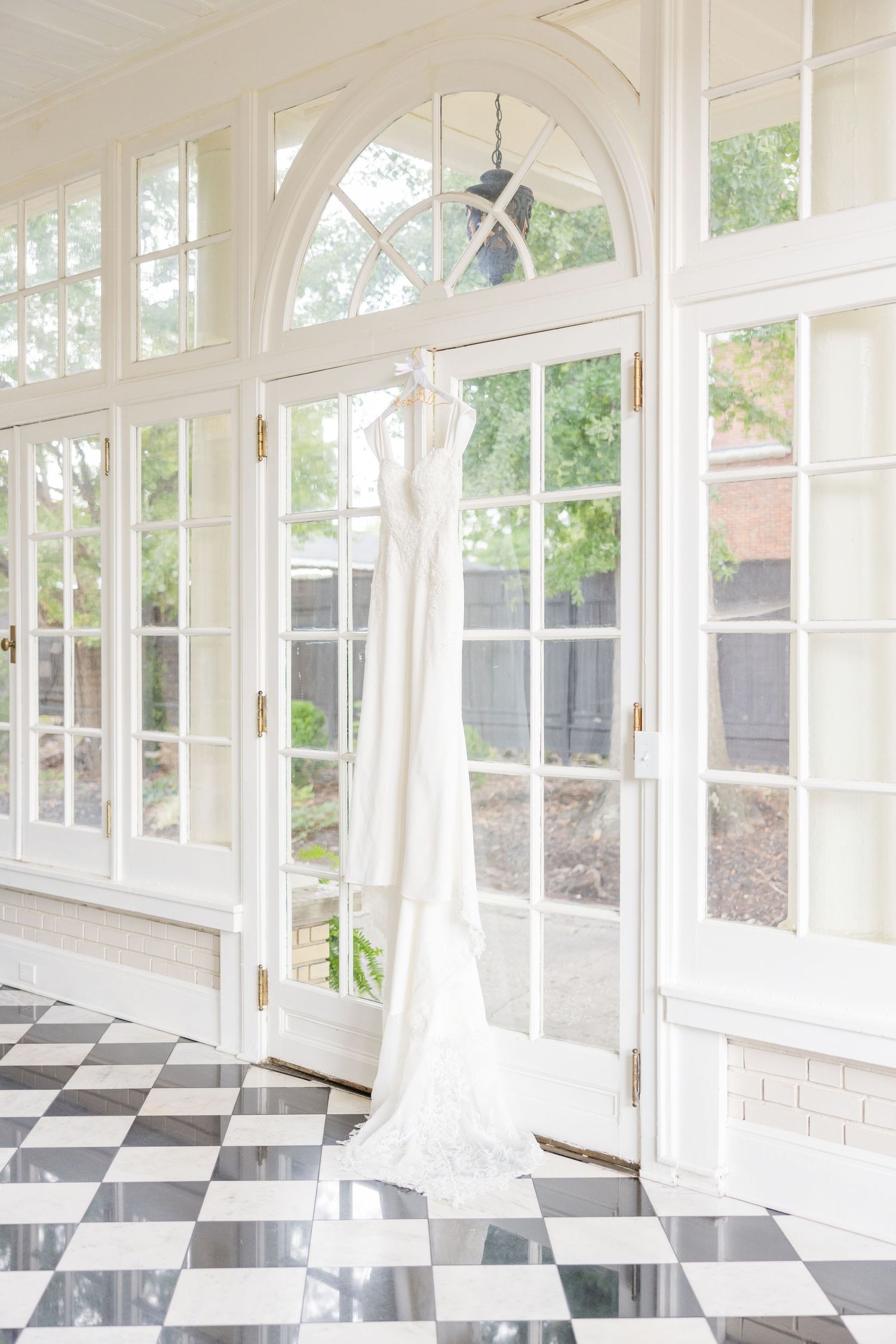 Elegant white conservatory with checkerboard floor and flowing wedding dress displayed.