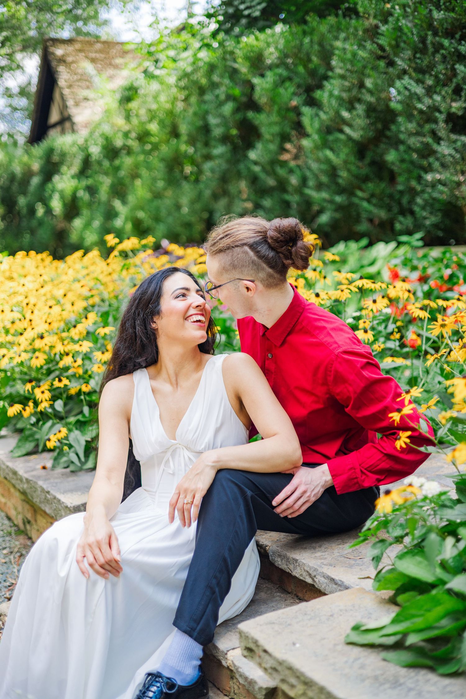 A couple shares tender moments while sitting on stone steps surrounded by yellow and orange flowers.