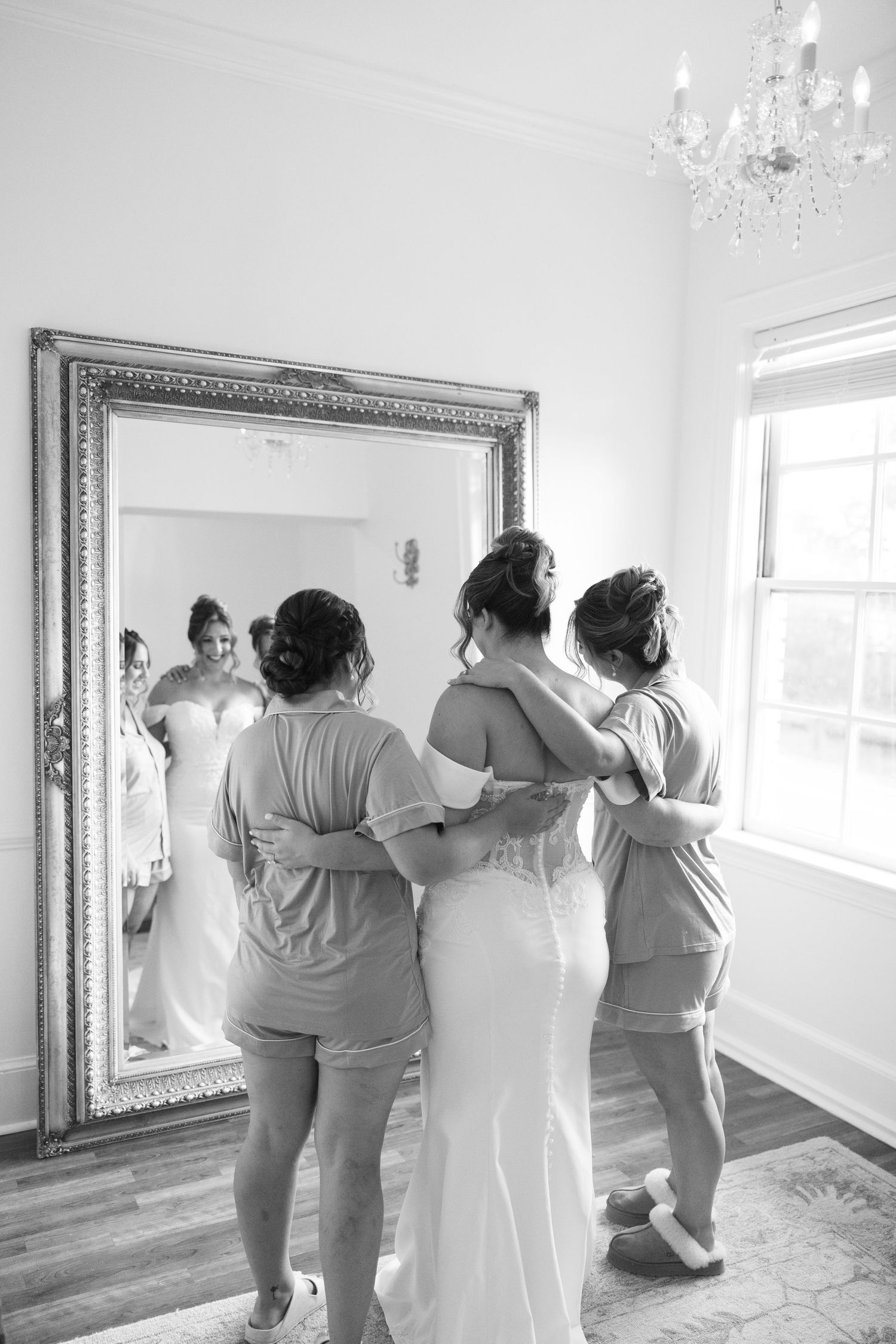 Wedding party helps with final preparations in a bright white room with an ornate mirror.