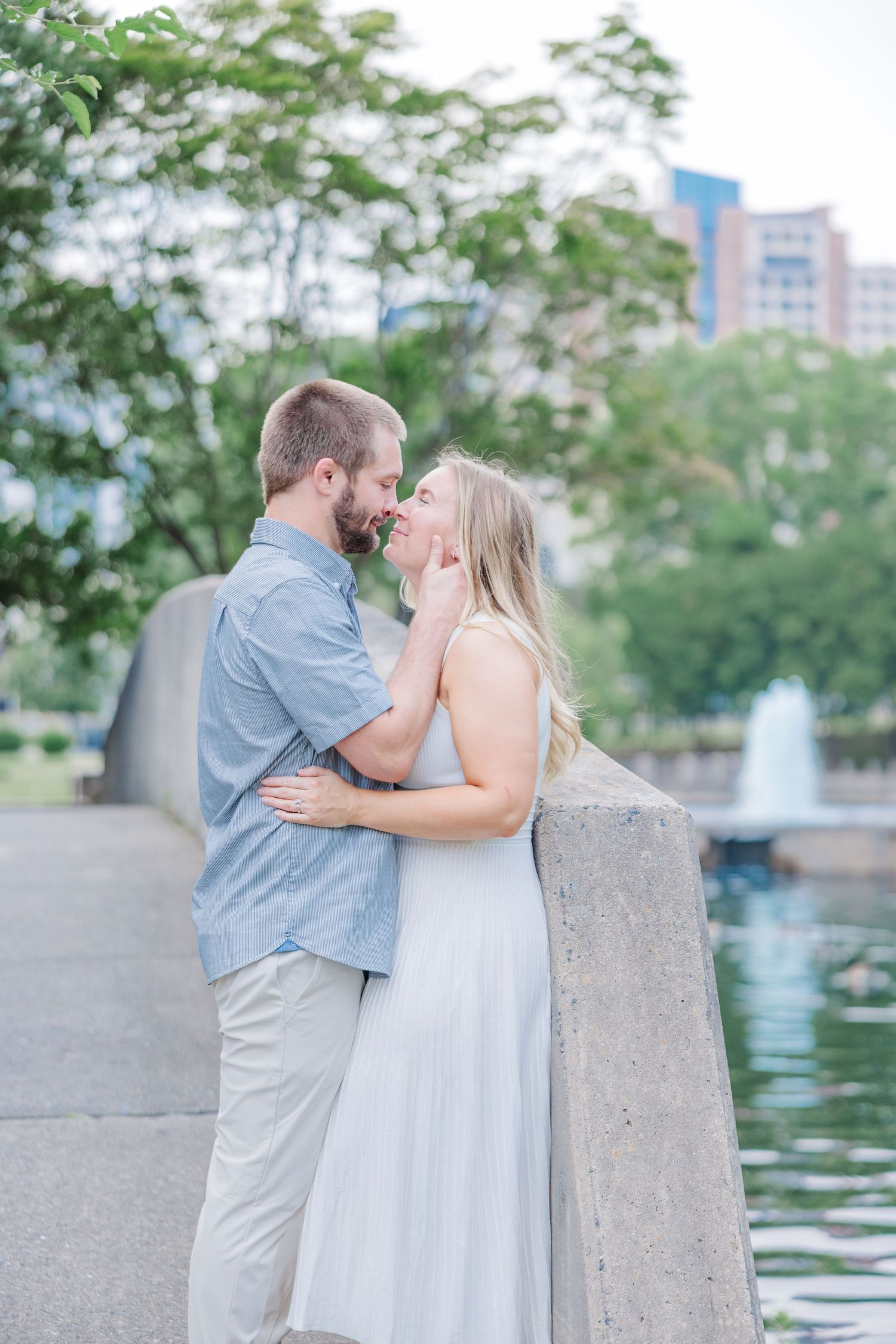 Romantic couple poses by waterfront fountain during outdoor engagement session.