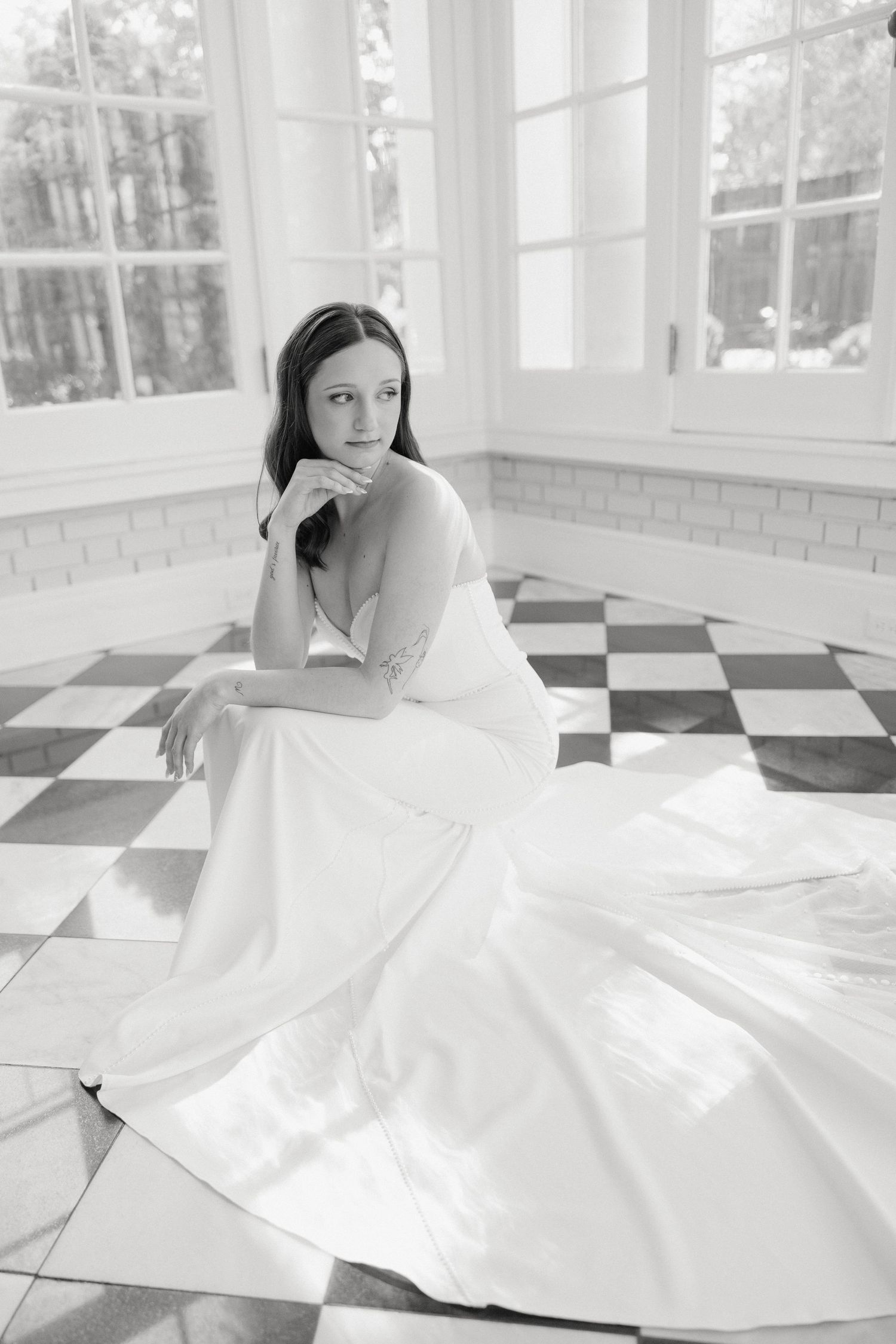 Elegant bridal portrait on checkered floor in sunlit room with flowing white gown.
