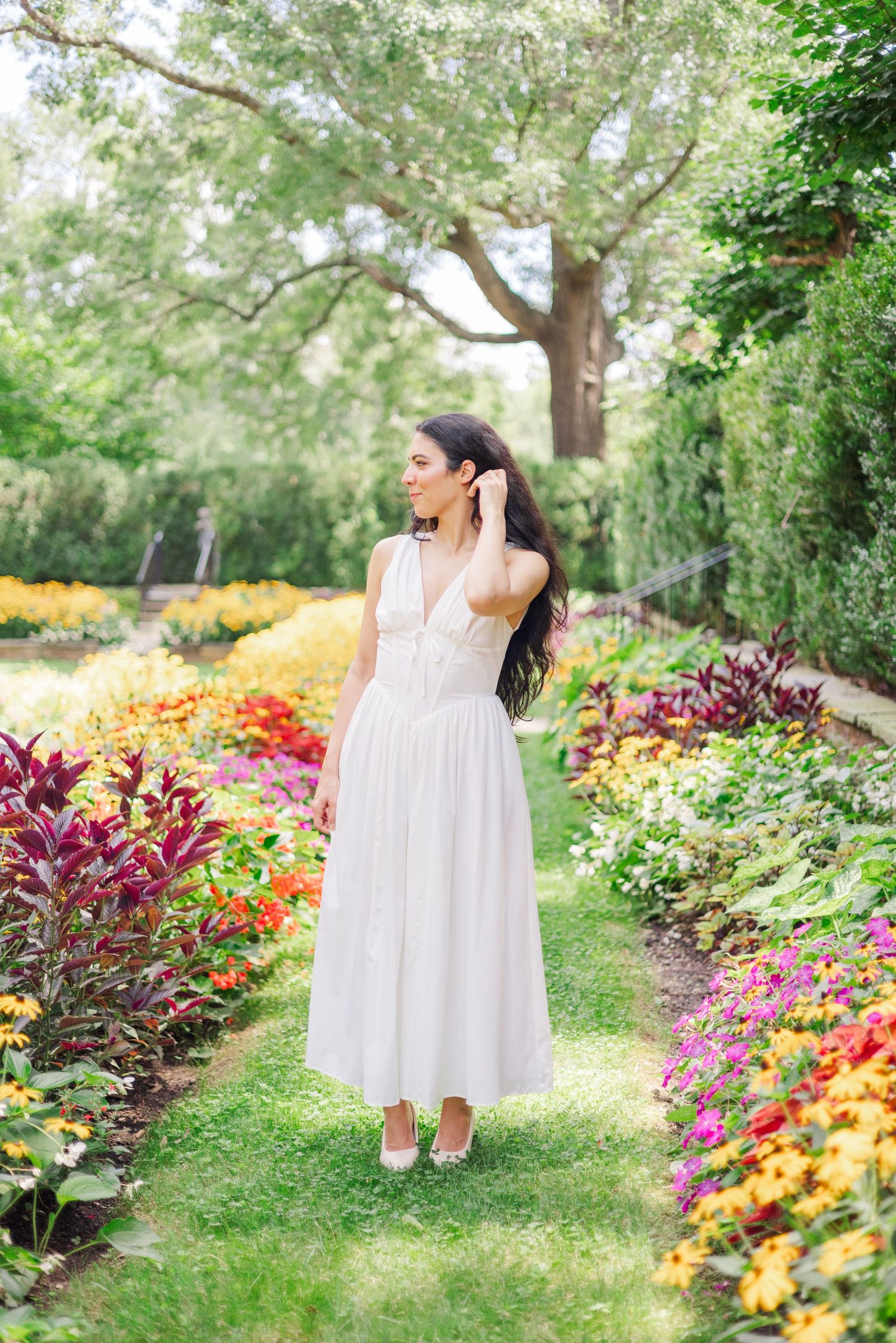 A person in a flowing white dress walks through a vibrant garden path filled with colorful flowers.