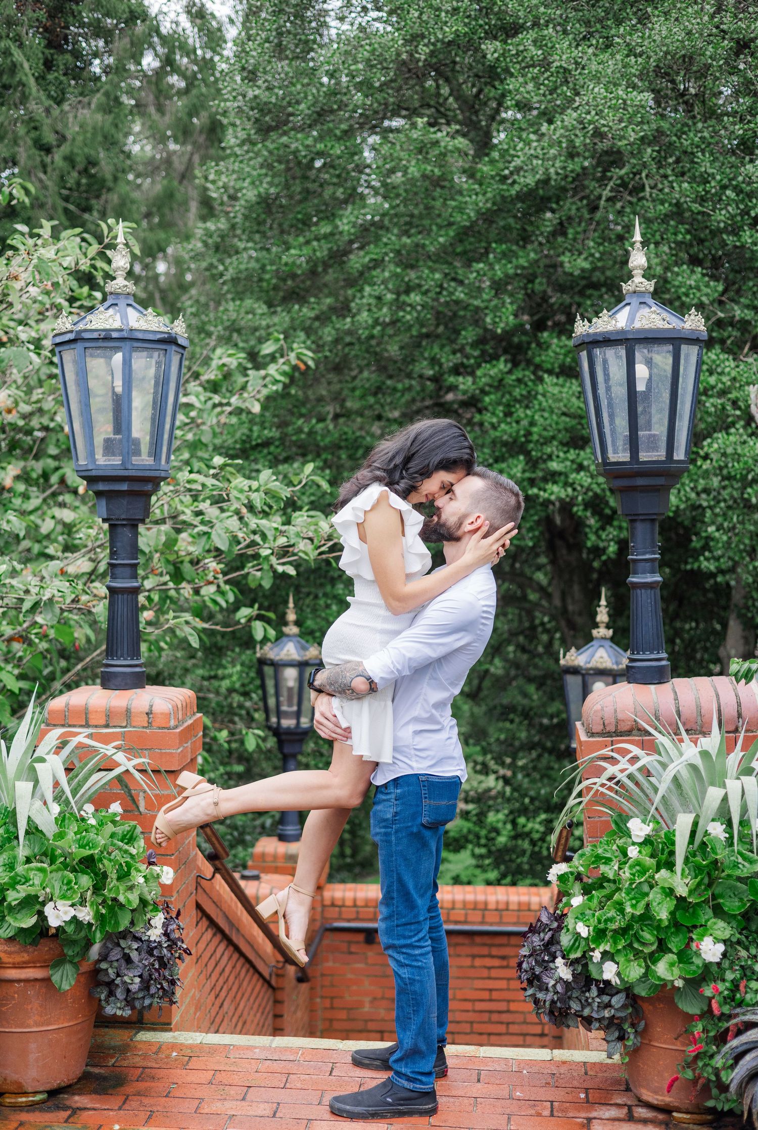 A romantic moment between a couple by decorative lamp posts and potted plants on a brick patio.