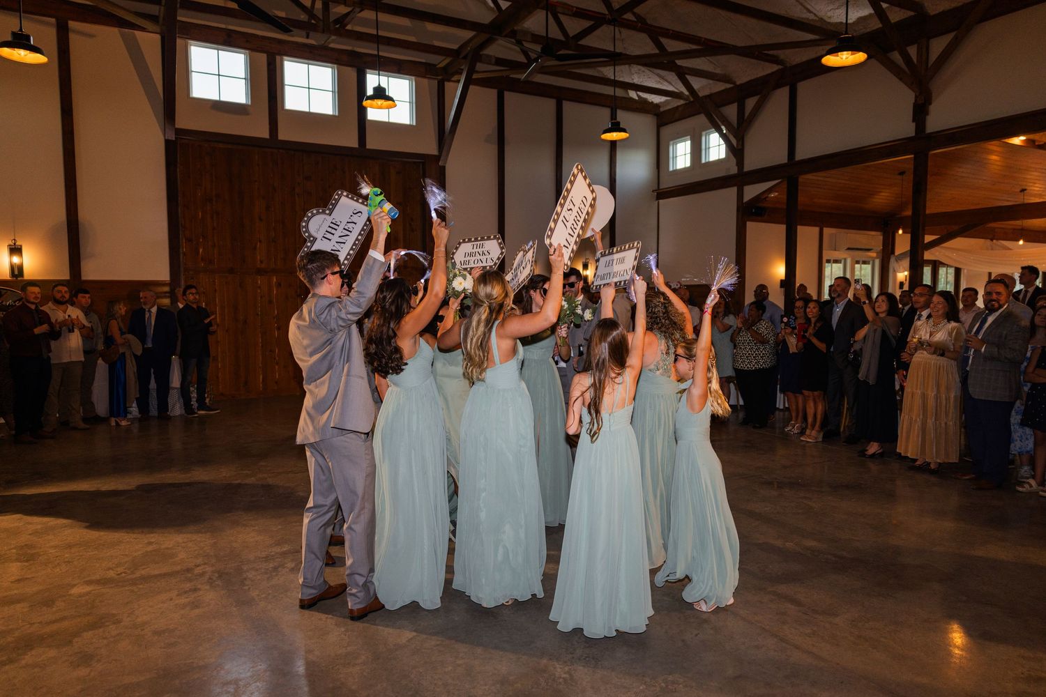 Wedding reception guests dance and celebrate in a rustic barn venue with high ceilings.