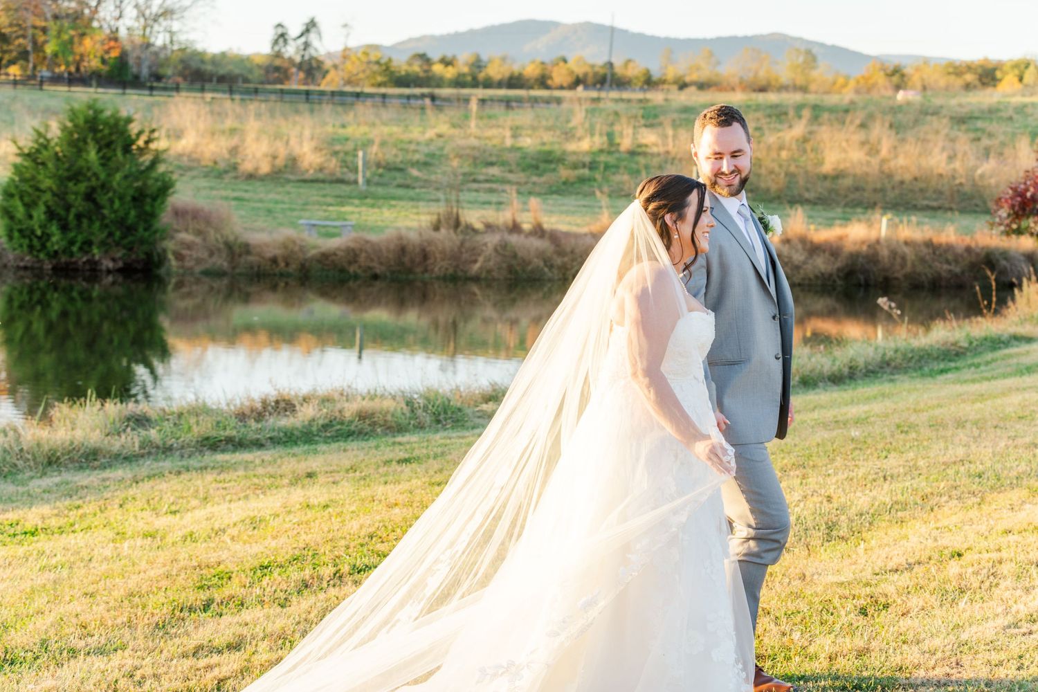 Newlyweds walk hand in hand through a sunlit field at golden hour.