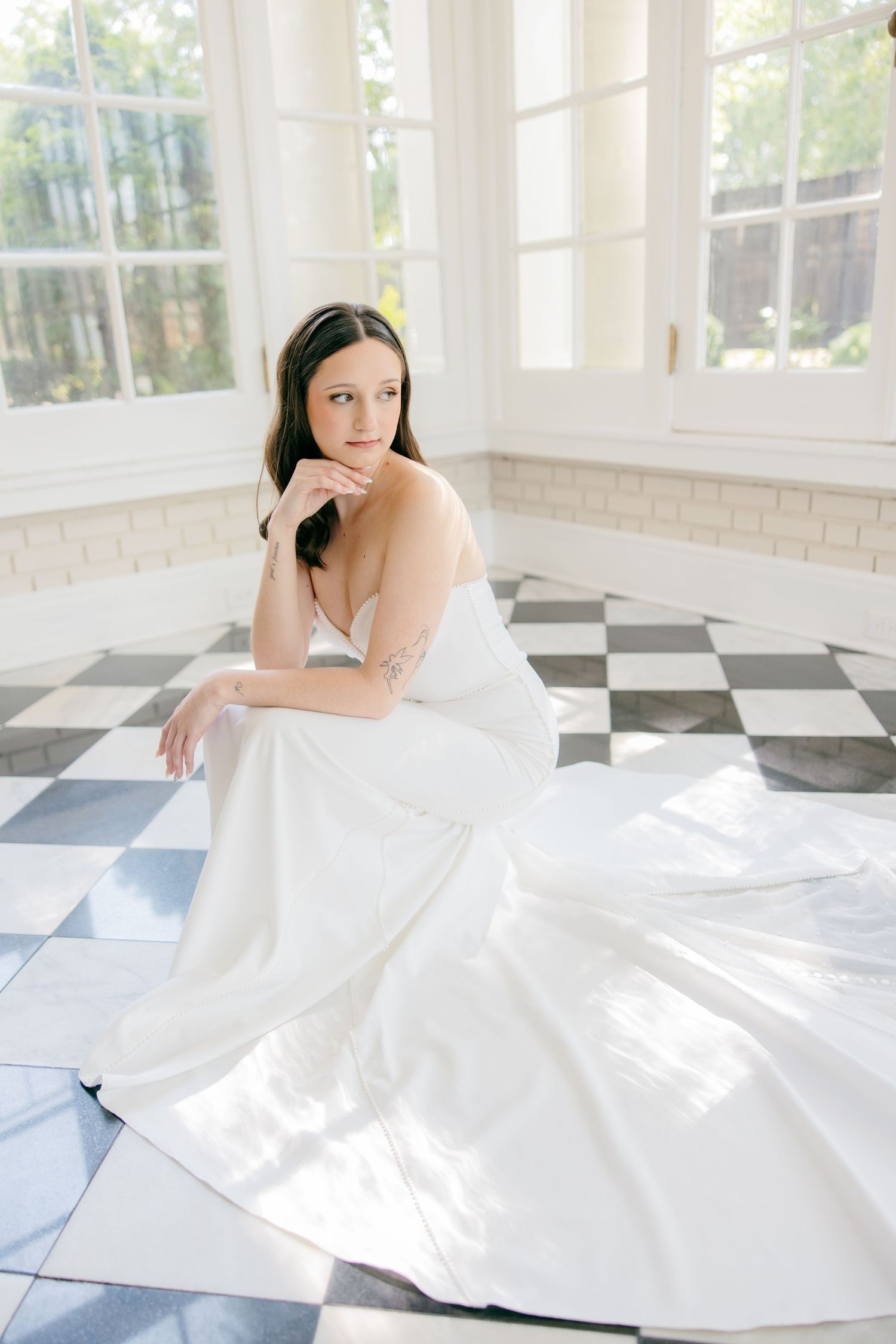 A white wedding gown spreads out in elegant motion across a checkerboard floor.