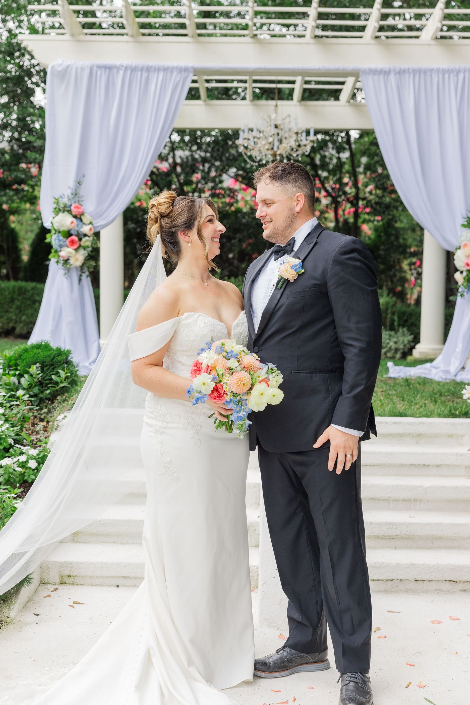 Wedding couple sharing intimate moments under a white draped outdoor gazebo.