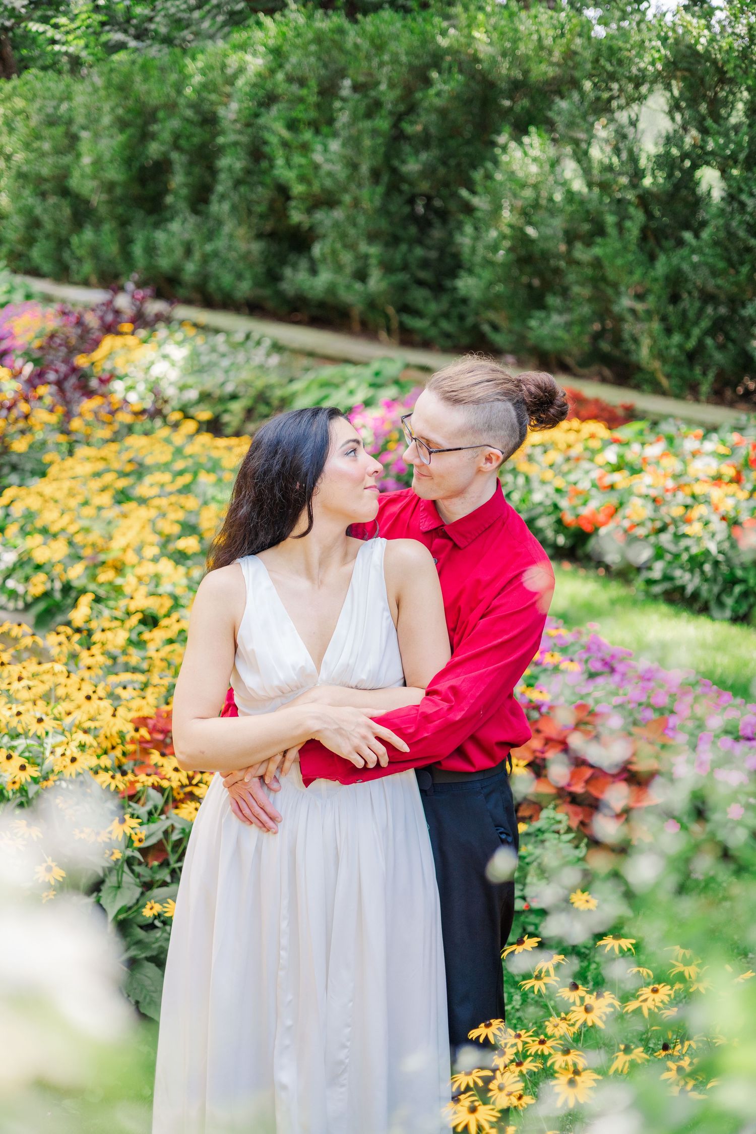A couple embraces in a colorful flower garden on a sunny day.