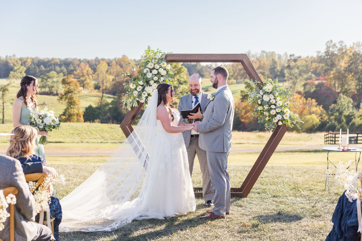 Wedding ceremony setup in an autumn field with wooden arch and floral arrangements.