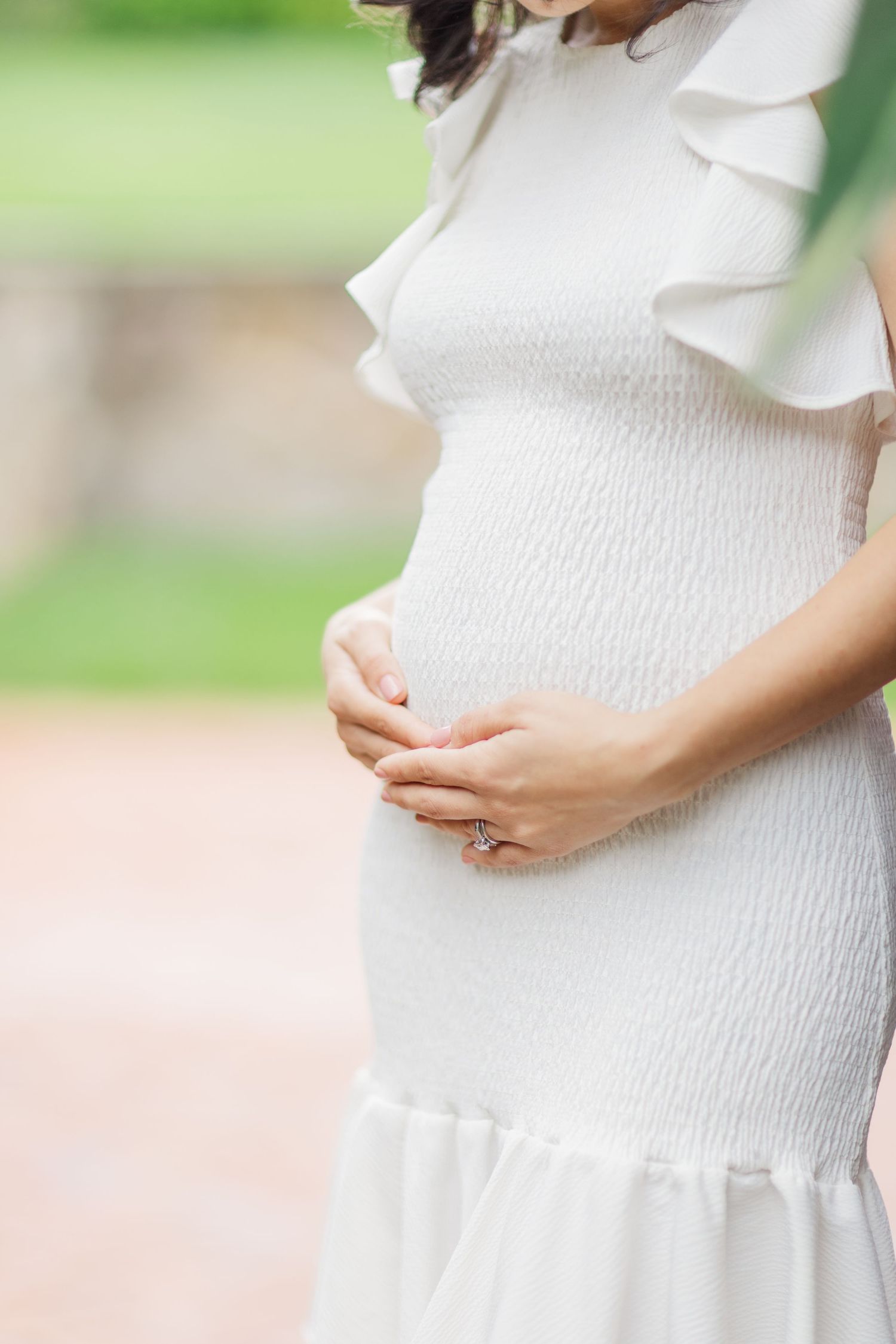 Close up of a pregnant woman's belly in a white textured dress with hands gently resting on her stomach.