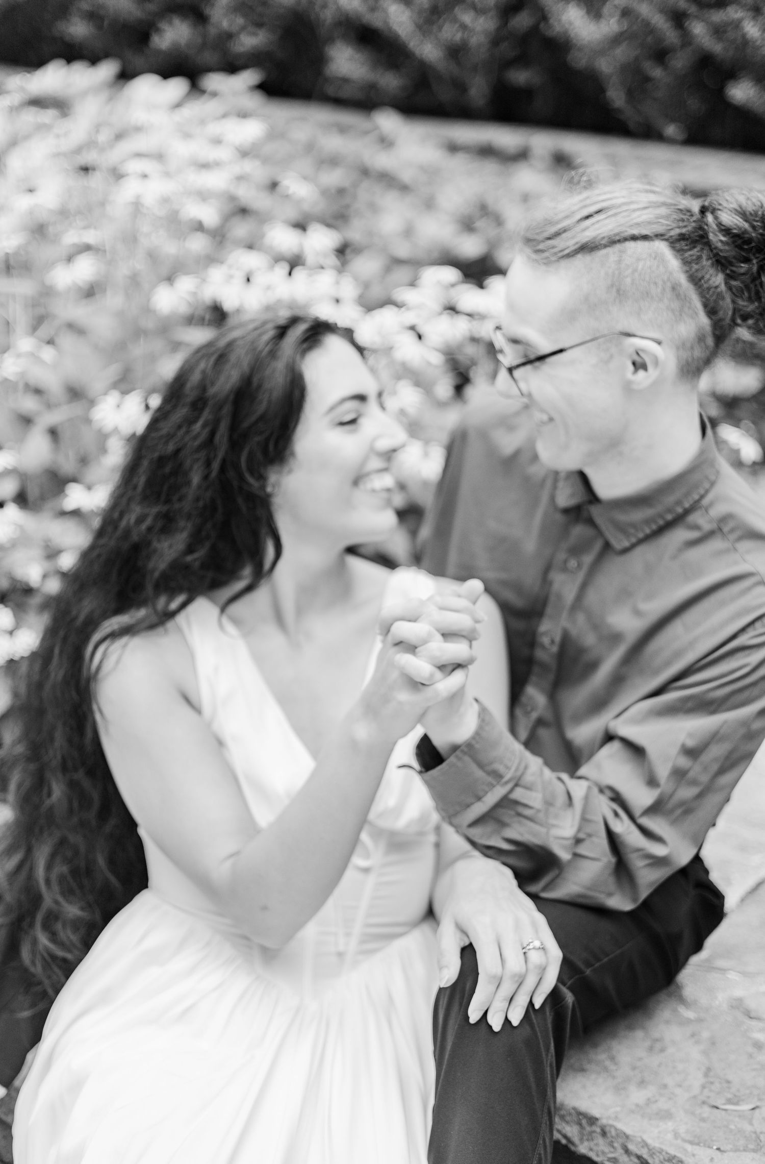 A black and white photo captures a couple sharing a candid laughing moment outdoors.