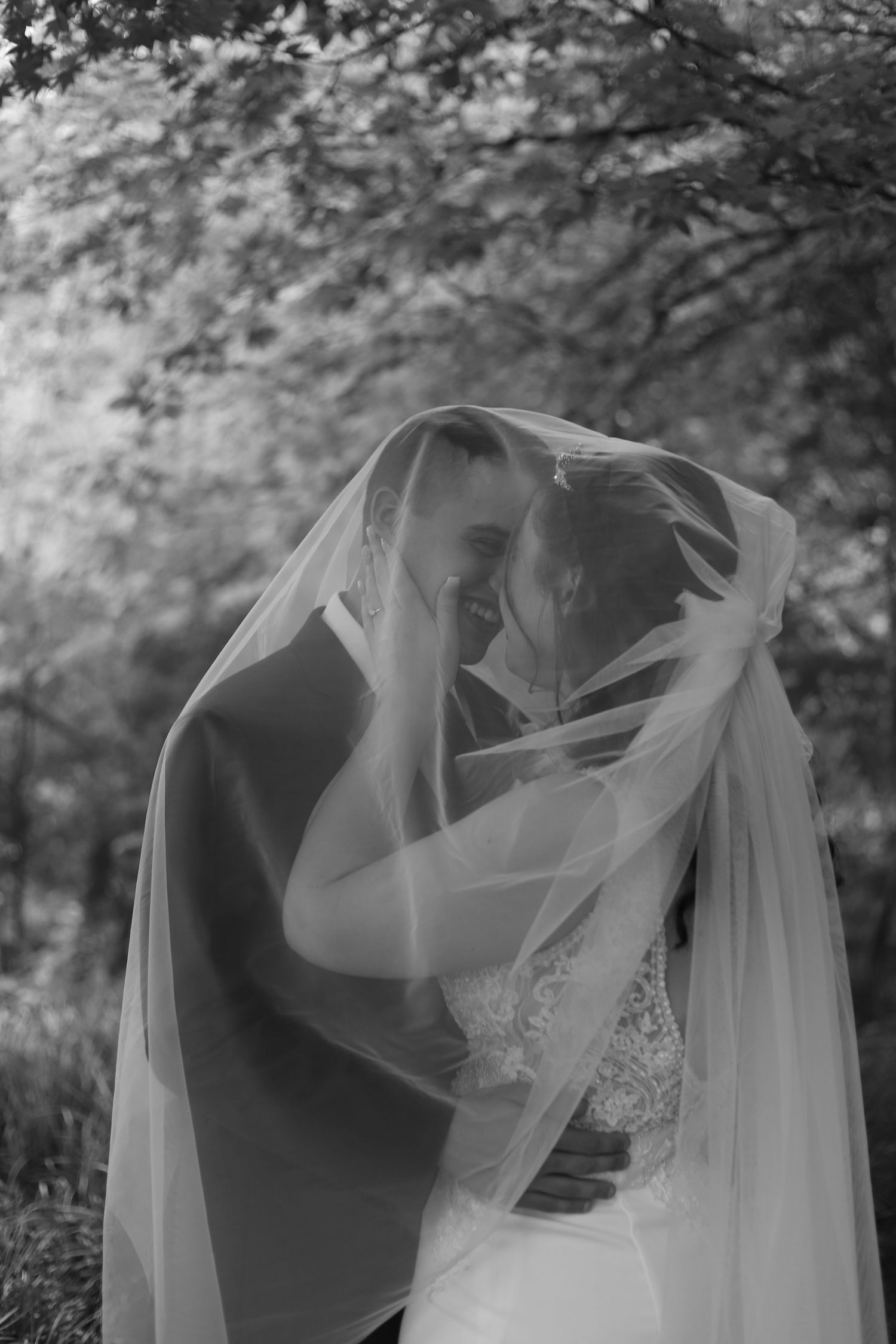Romantic black and white photo of couple sharing an intimate moment under bride's veil.
