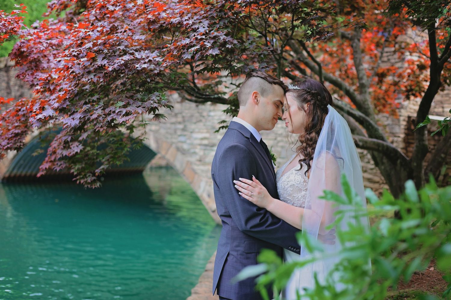 A couple shares a romantic moment under vibrant red autumn foliage beside a turquoise lake.