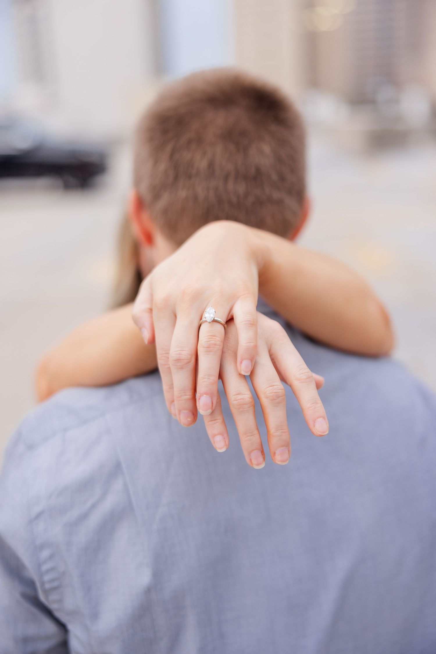 Close-up of hands displaying engagement ring against a gray shirt.