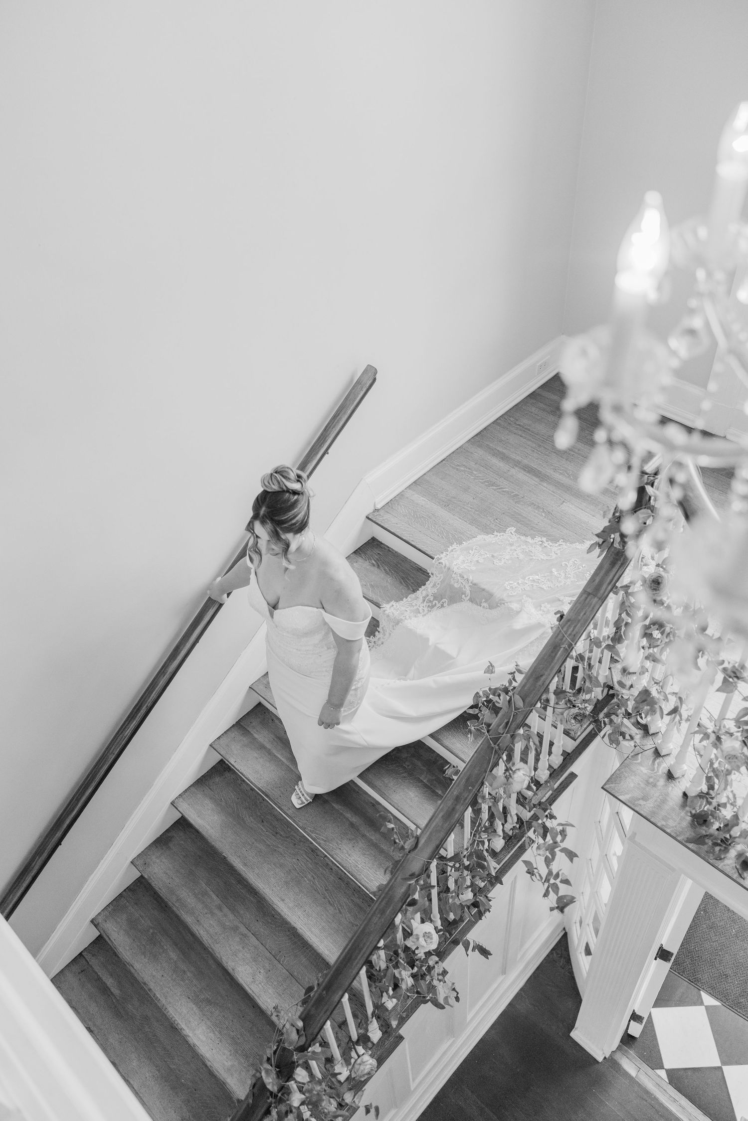 A bride in white descends an elegant staircase decorated with floral arrangements in black and white.