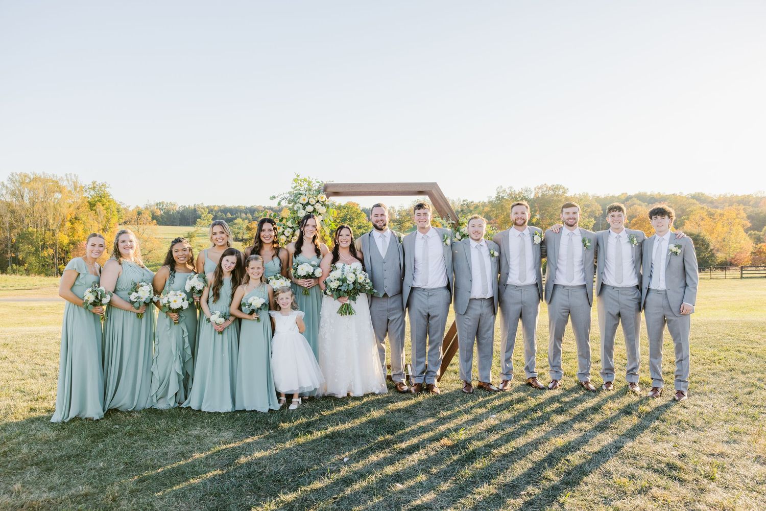 Wedding party in sage green and grey attire lined up creating long shadows in evening sunlight.