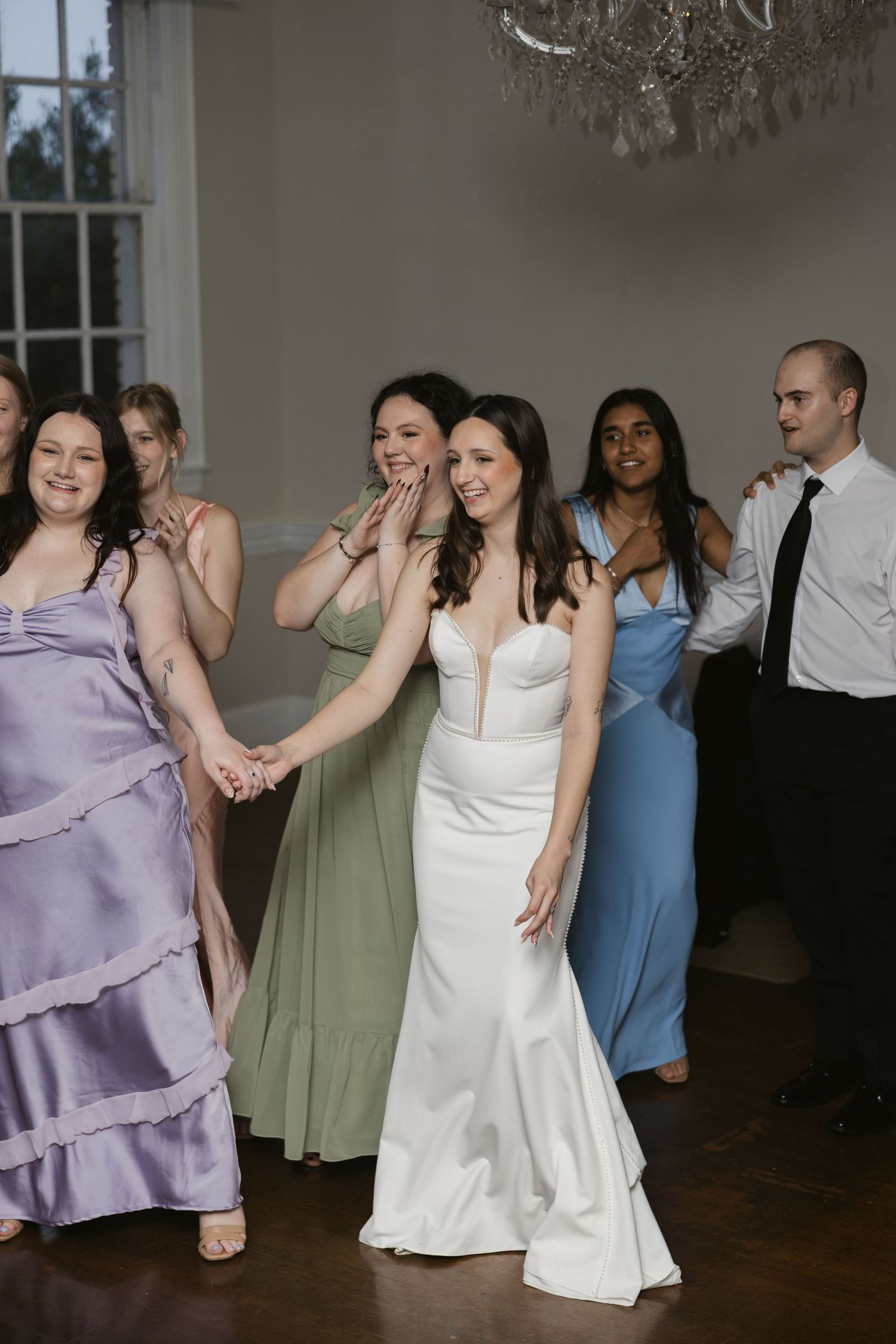 Wedding guests and bridal party dancing and celebrating in an elegant reception room with a crystal chandelier.