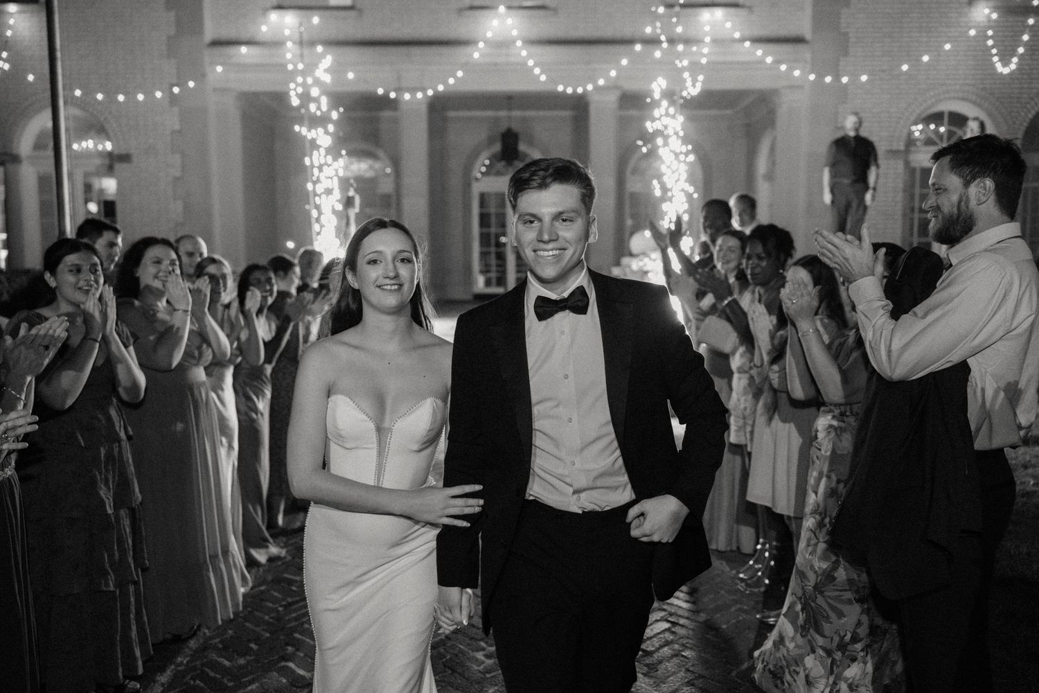 Wedding reception guests dancing and celebrating on a dance floor decorated with string lights.