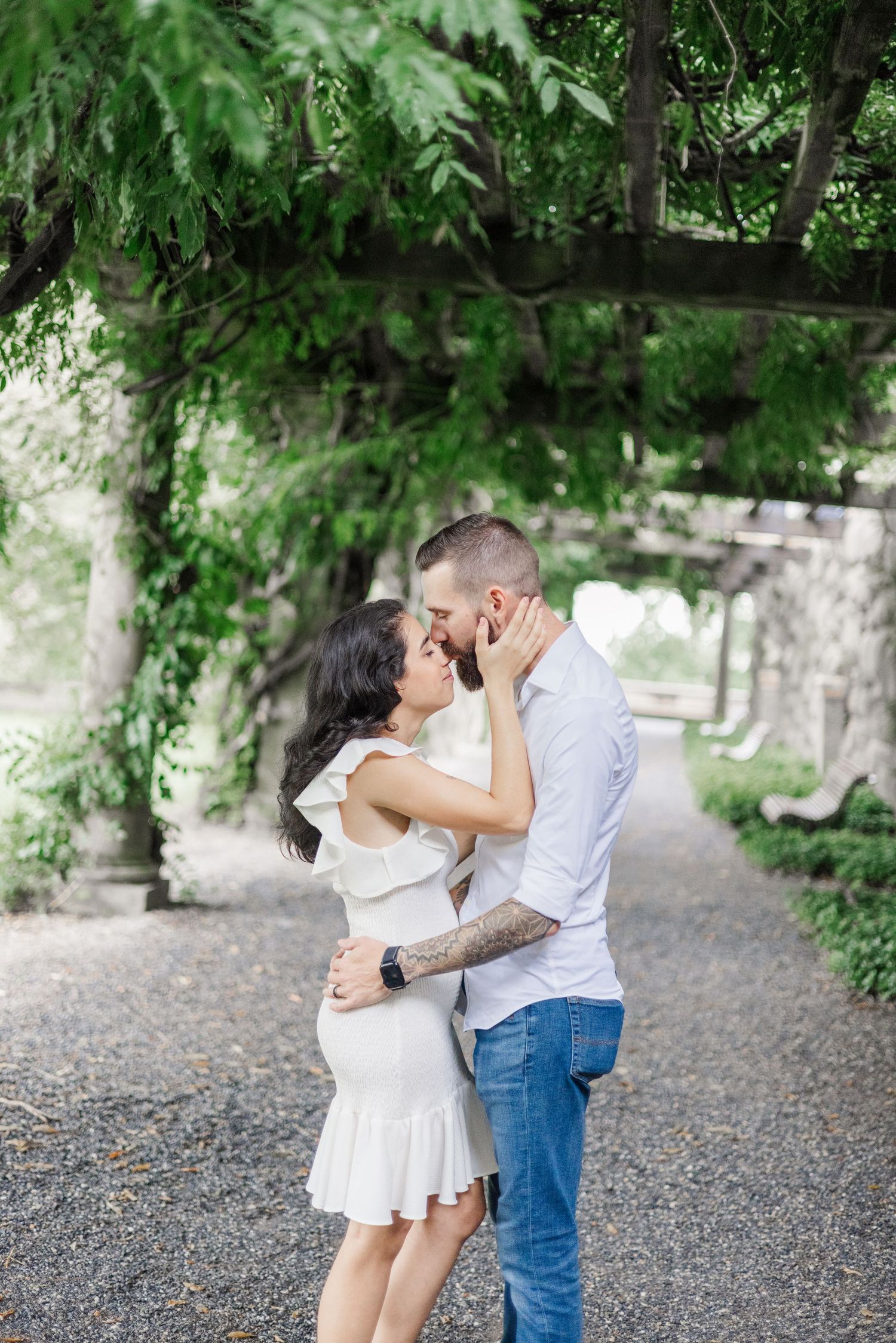 Romantic moment captured on a gravel path under green foliage and stone walls.