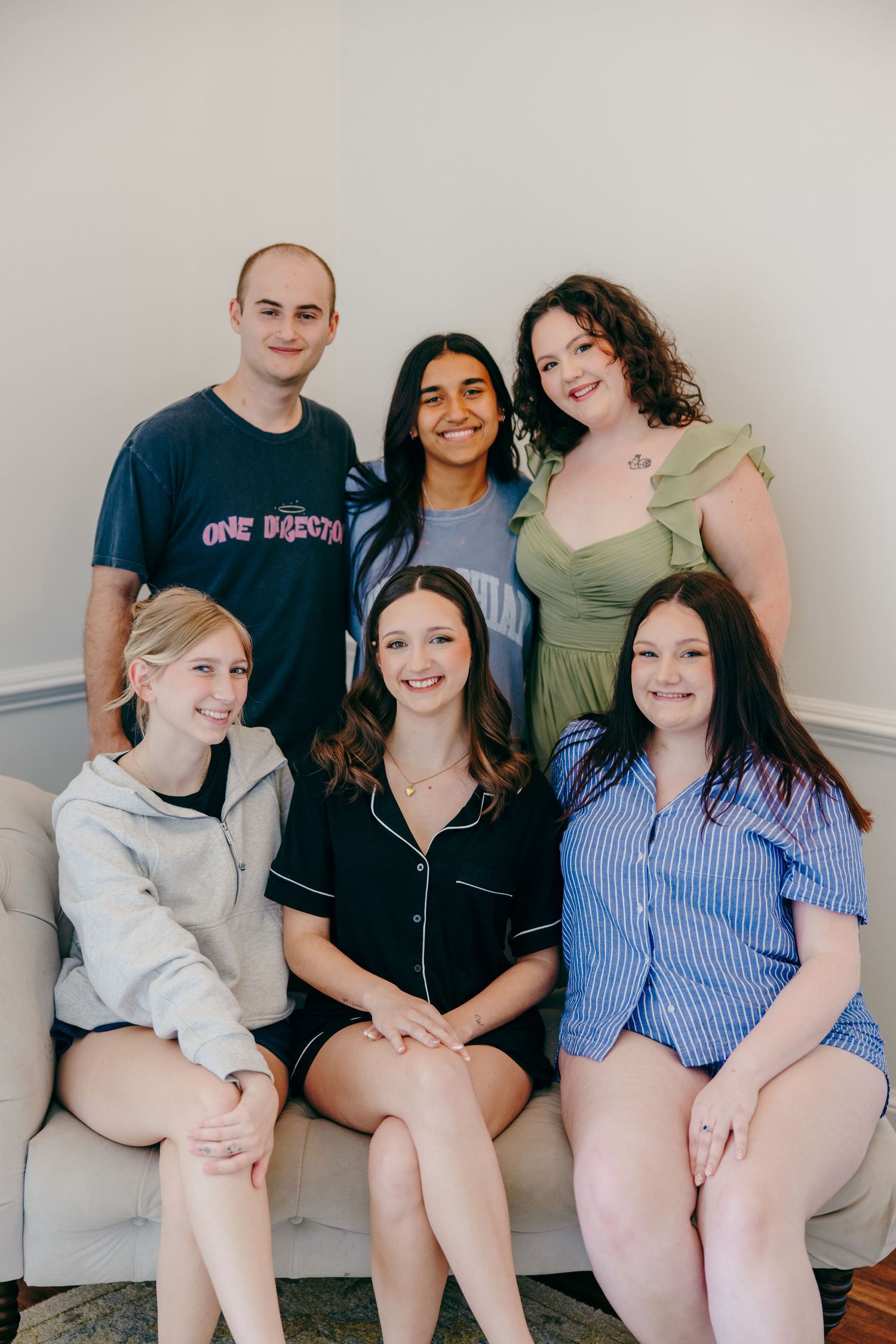 Group of friends in casual clothing sitting together on a white couch for informal portraits.