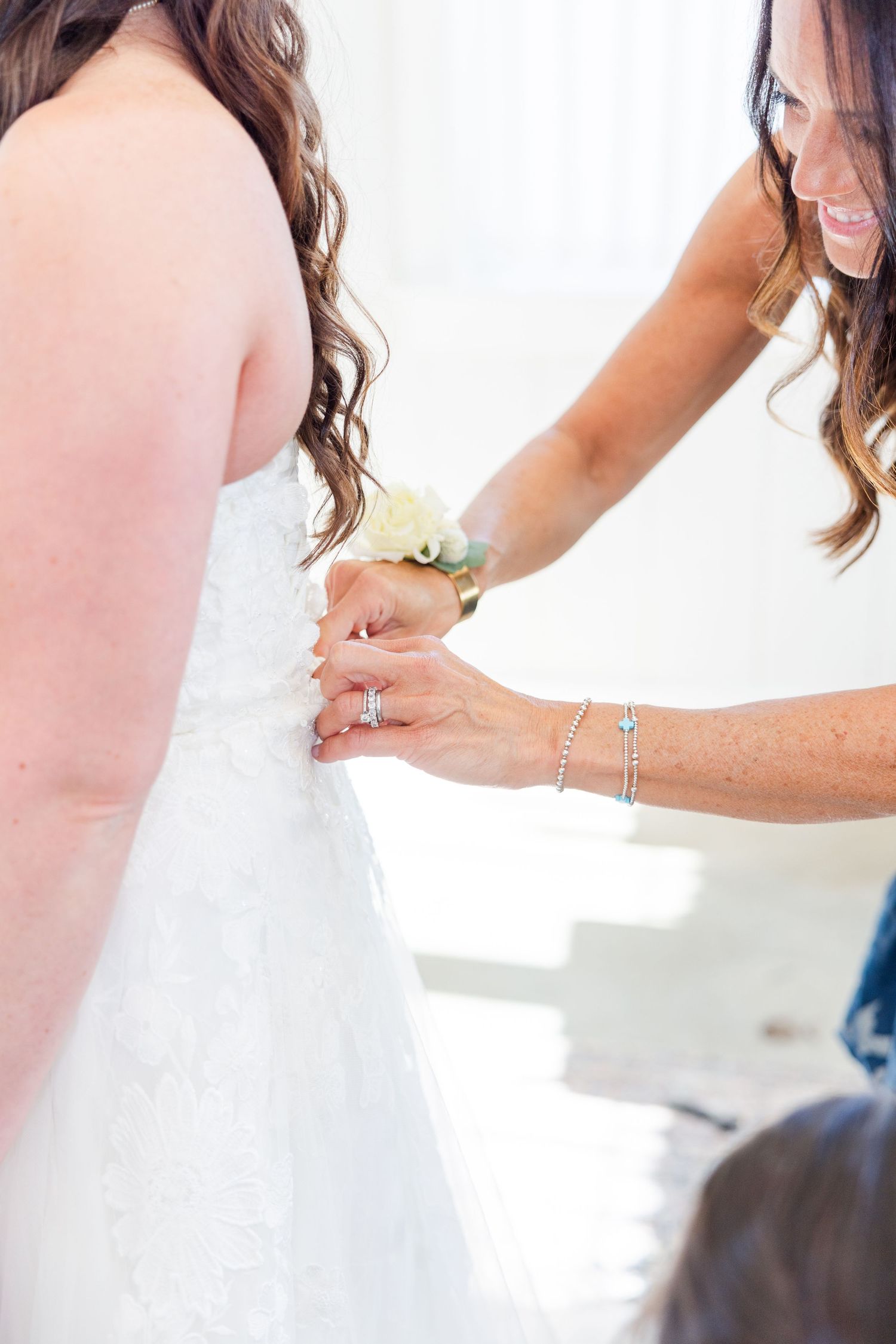 Close-up details of a white wedding dress being adjusted and fitted.