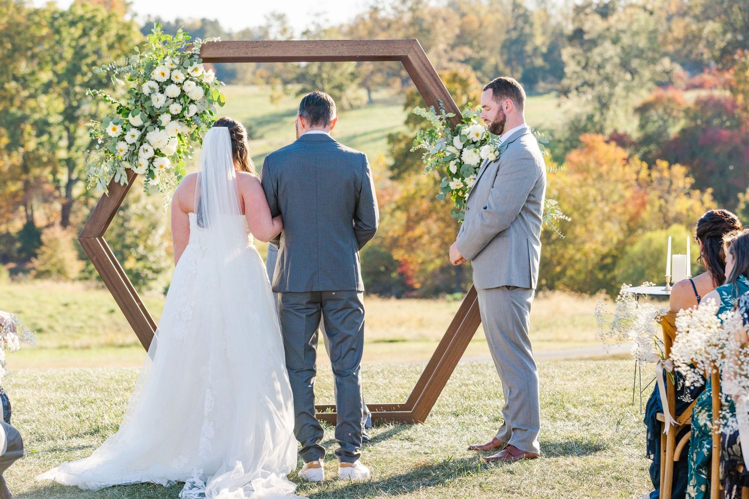 Outdoor wedding ceremony with wooden geometric arch and natural fall scenery.