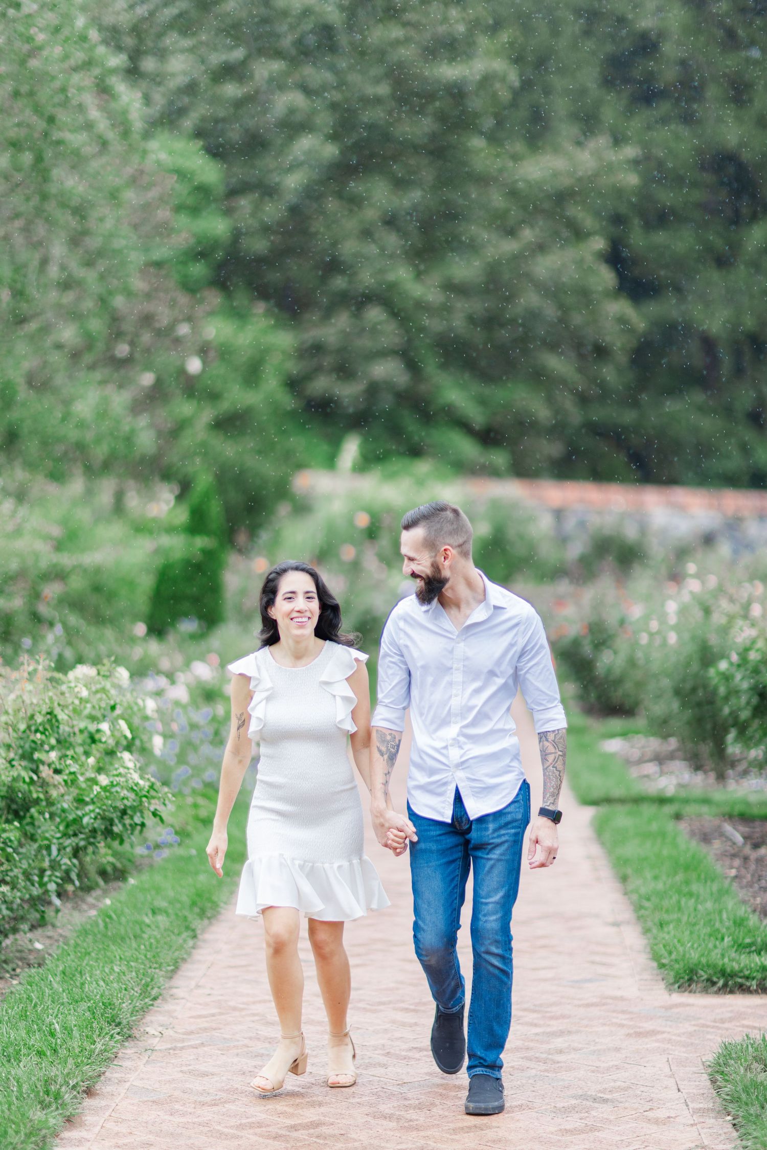 Couple walking along a brick pathway surrounded by flowering gardens.