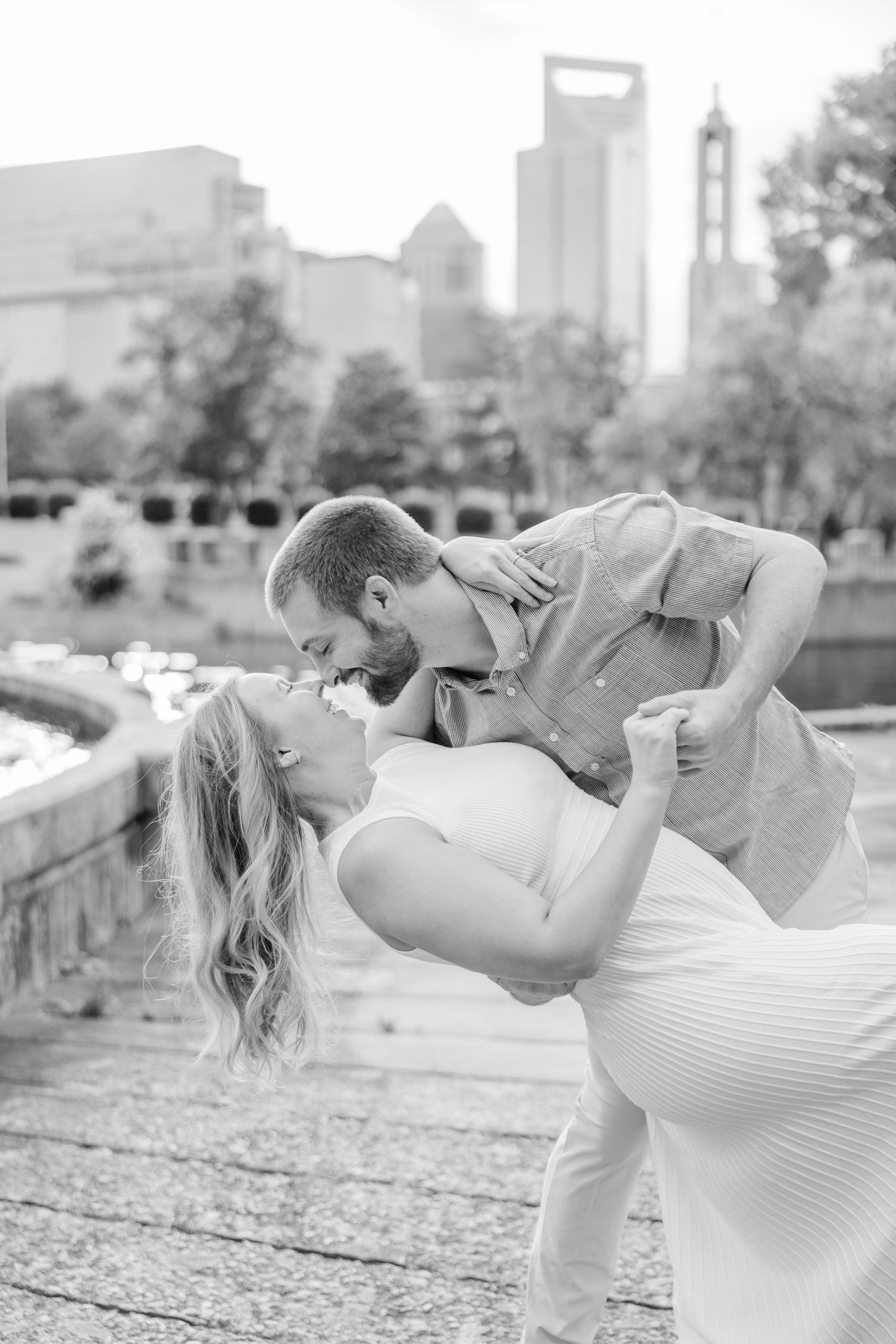 Black and white photo of a couple sharing a playful dip pose against a city backdrop.