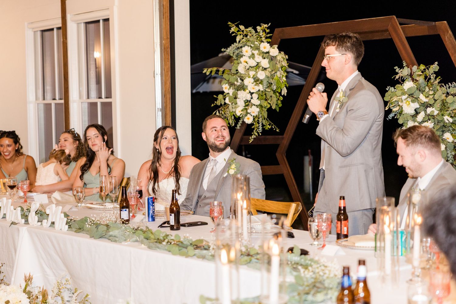 Wedding reception table decorated with floral arrangements and candles at night.