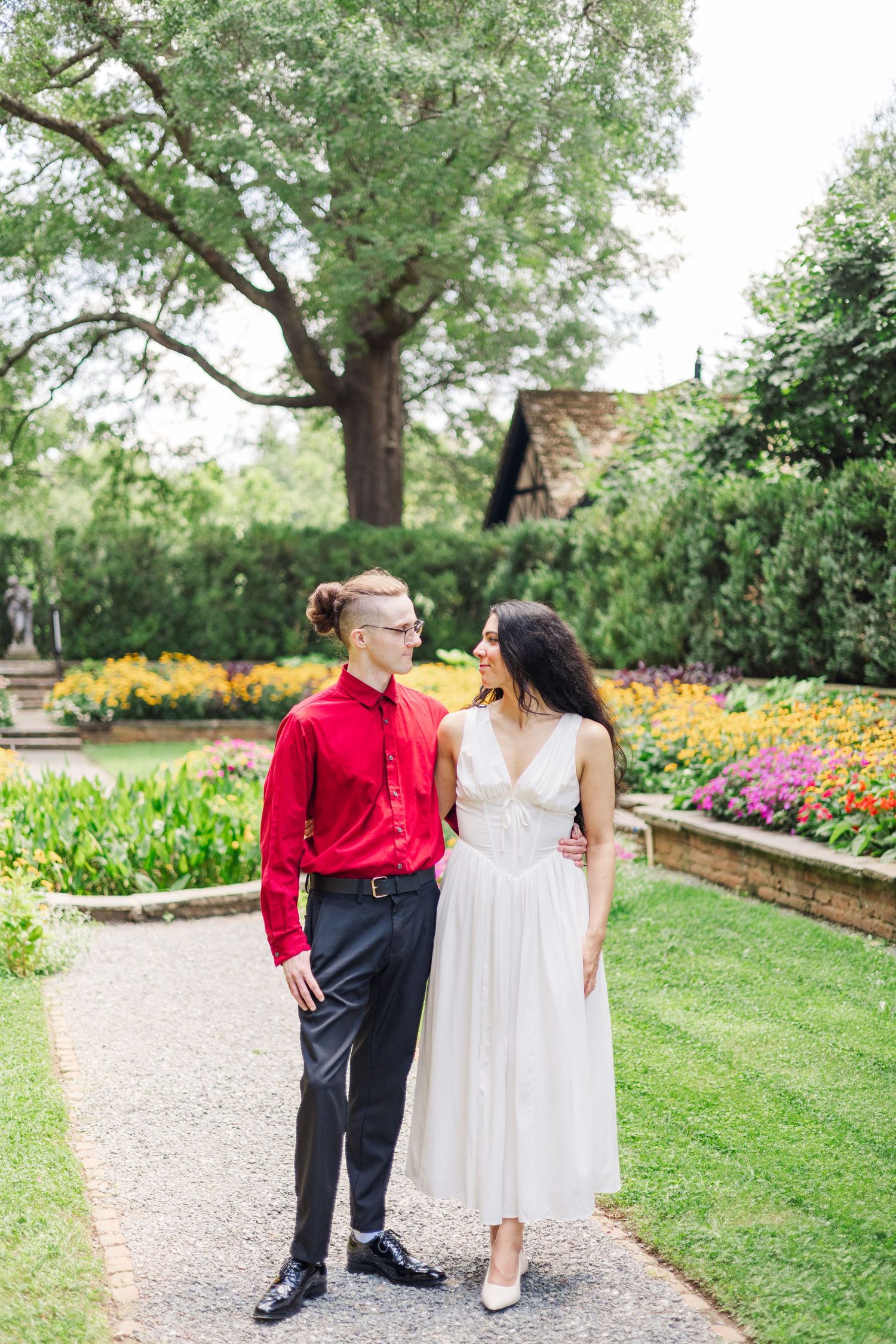 A couple walks together on a garden path surrounded by yellow and pink flowers.