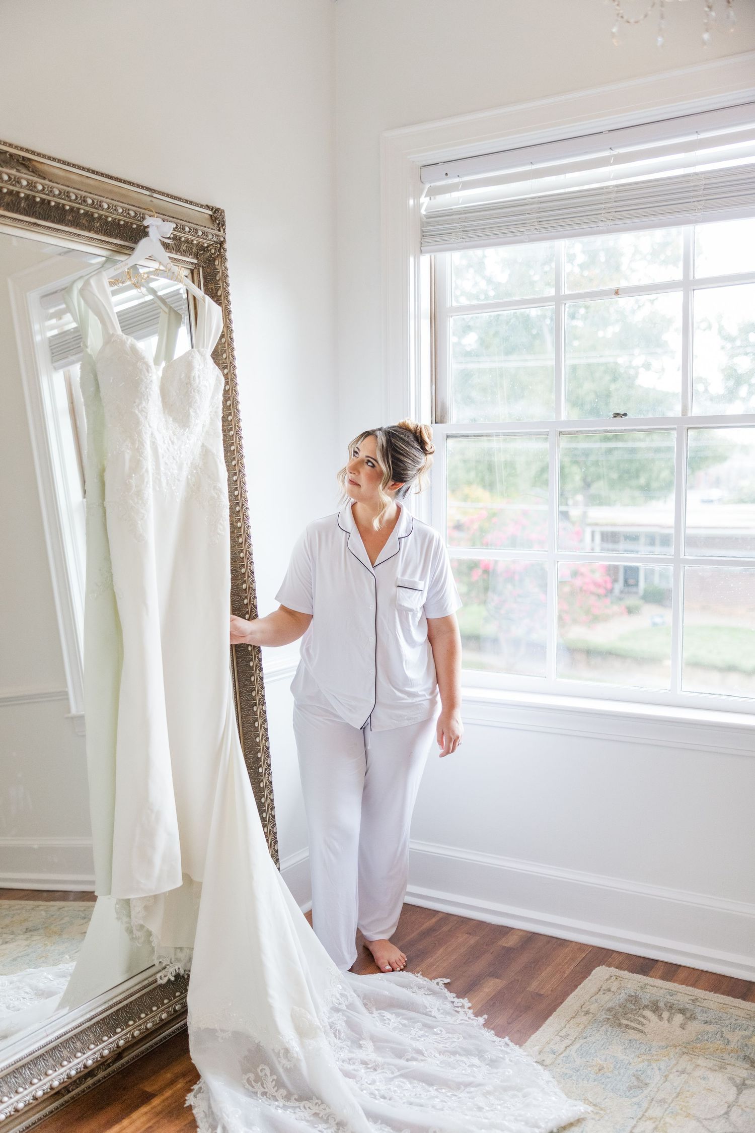 A wedding dress is displayed in a bright sunlit room with white walls and hardwood floors.
