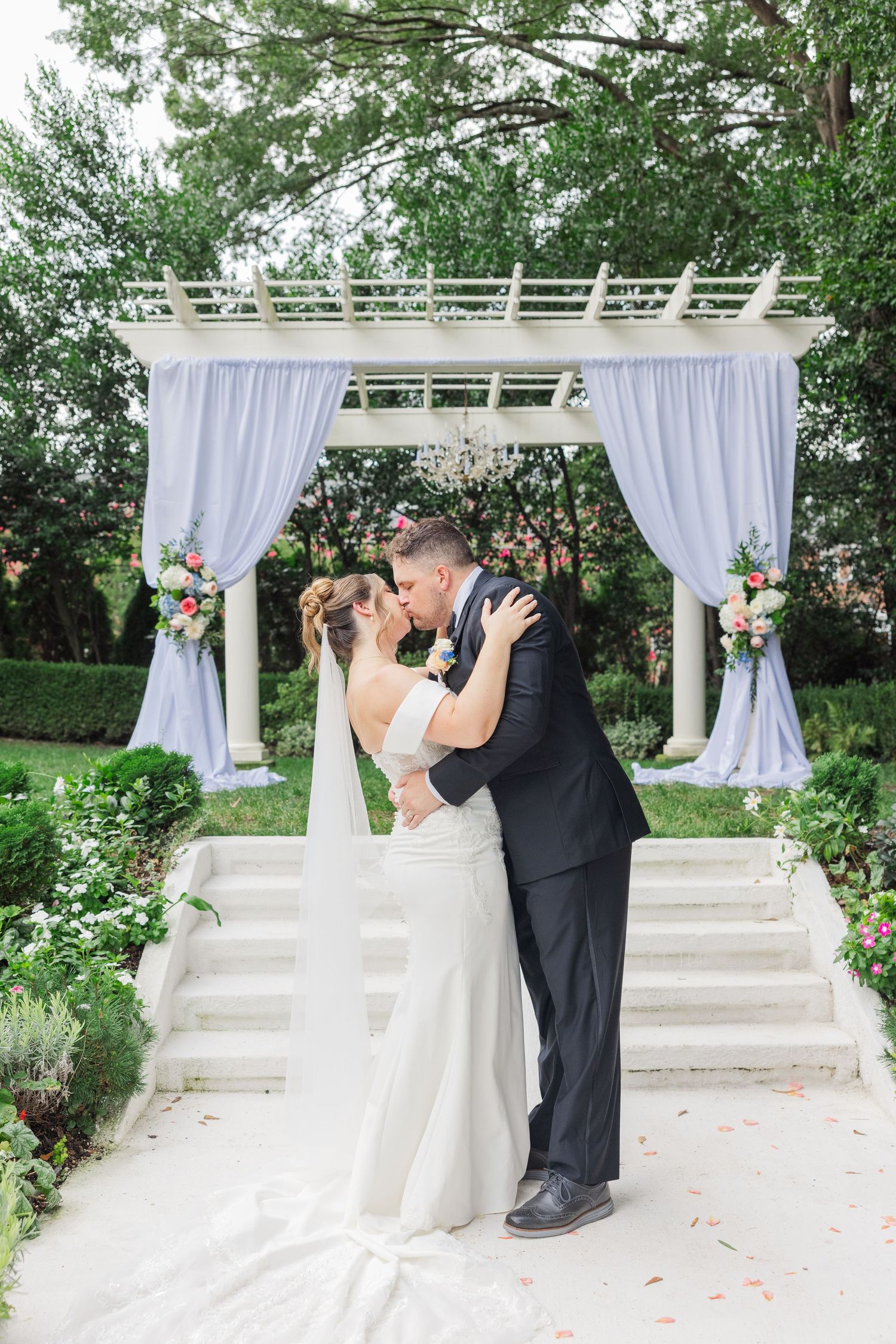 Romantic wedding ceremony under white pergola with flowing curtains and floral decorations.