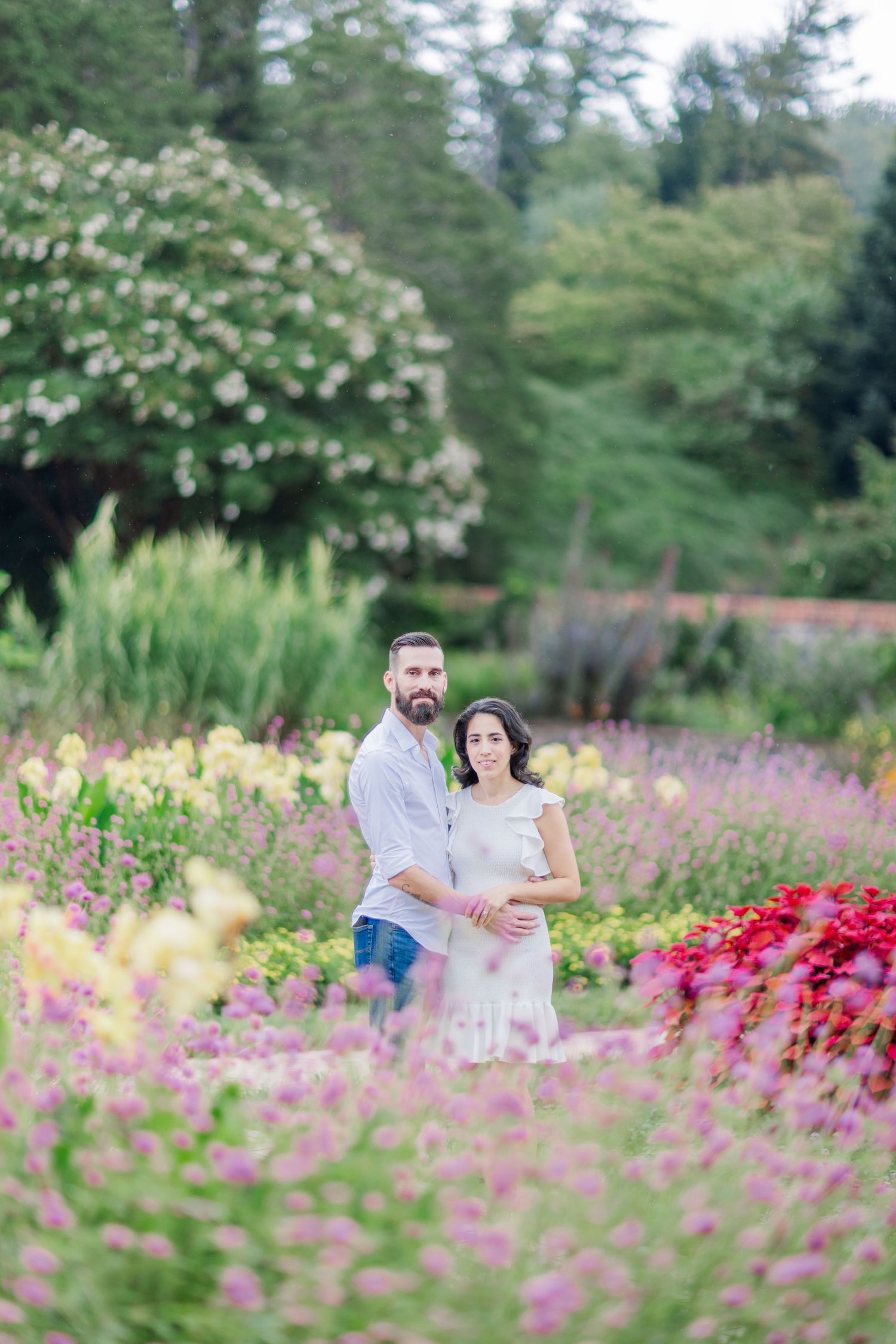 A couple poses together in a beautiful garden filled with pink and red wildflowers.