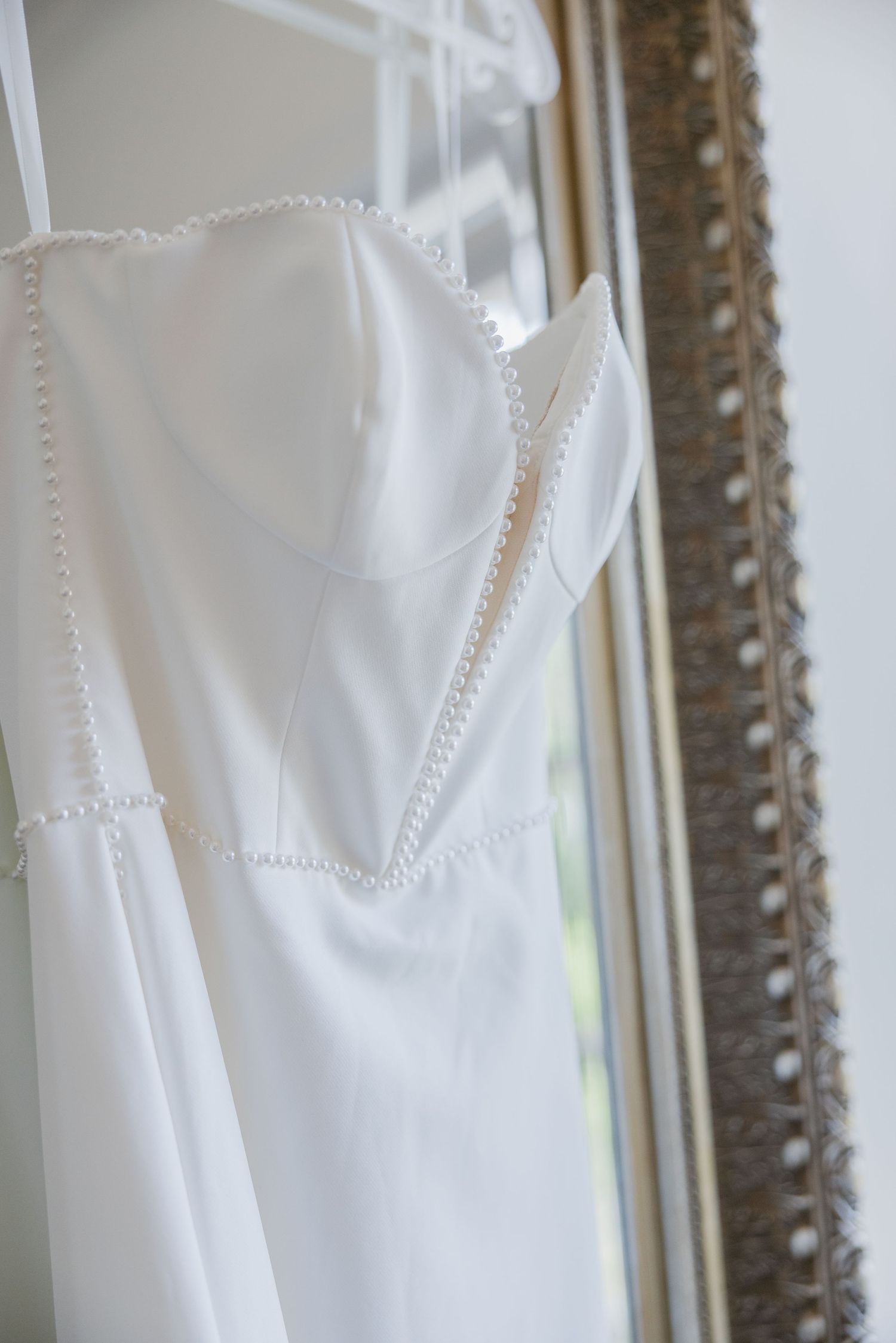 Close-up detail of white wedding dress fabric with delicate pearl beading and stitching.