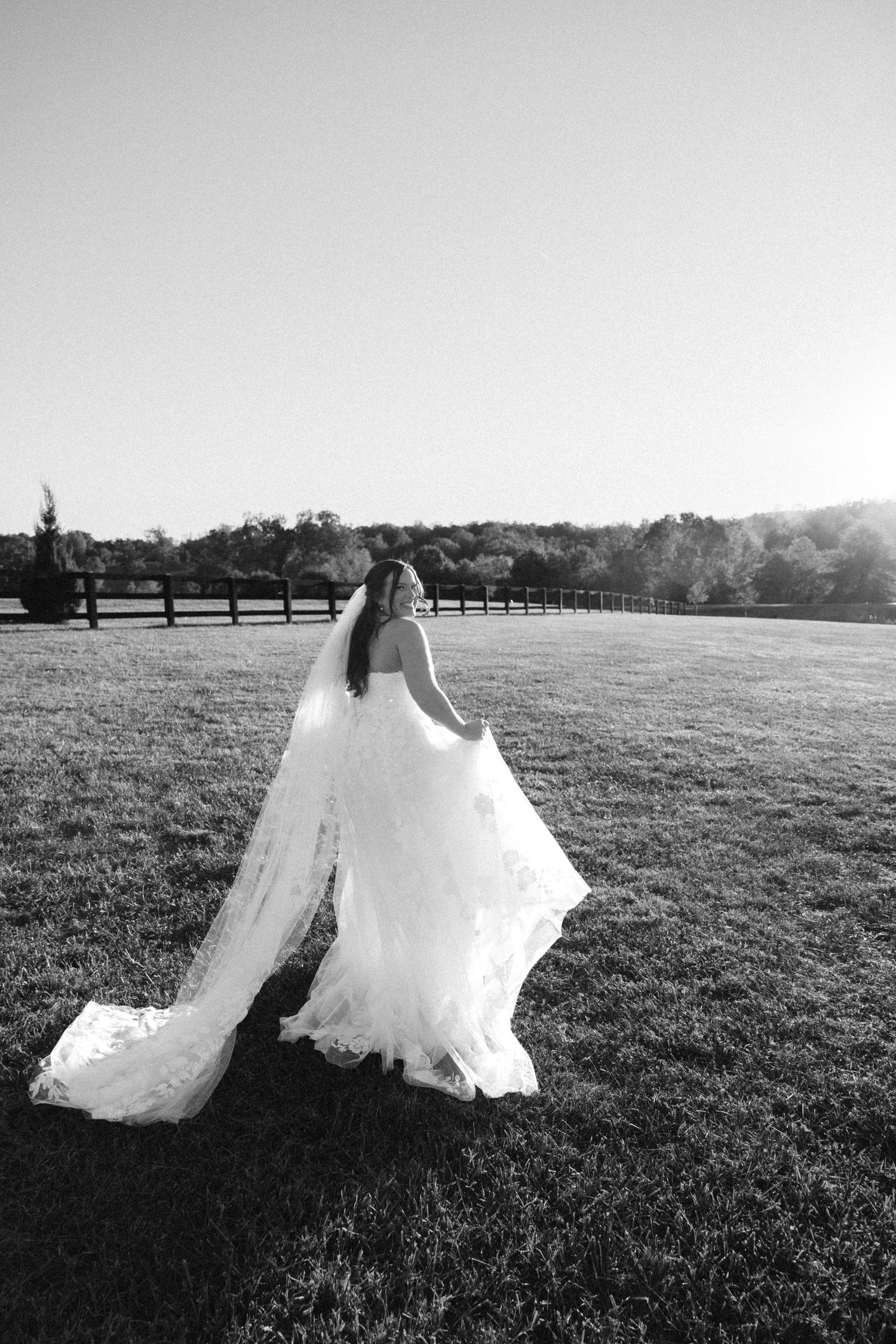 Black and white photos of flowing wedding dress movement in an open field with fencing.