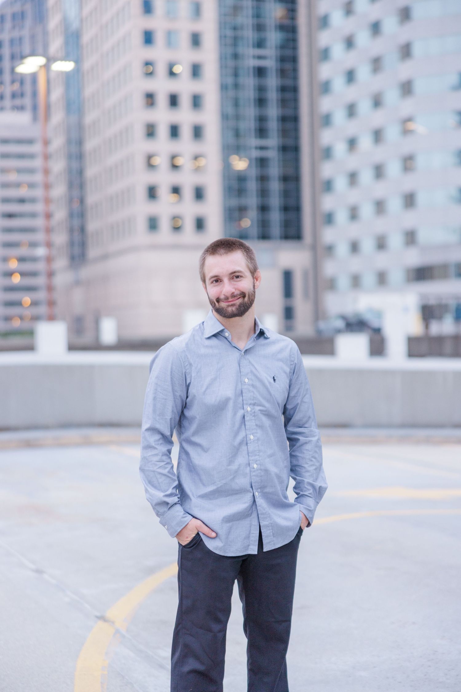 Professional standing in urban setting wearing business casual attire against modern office building backdrop.