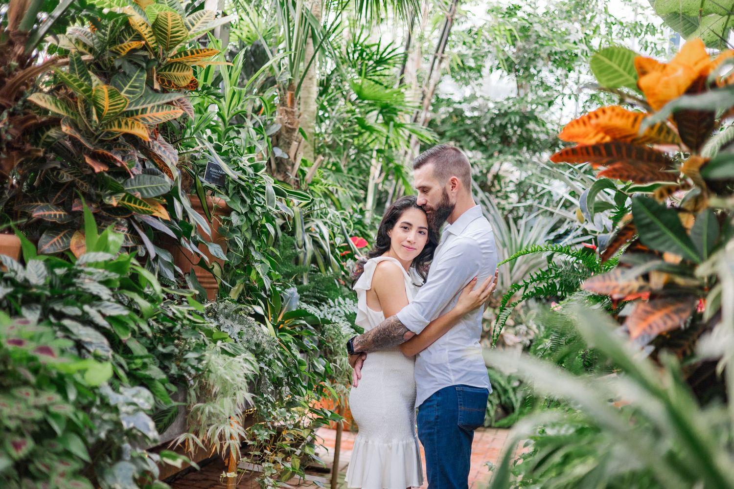 A couple embraces in a lush tropical garden setting with vibrant green foliage surrounding them.