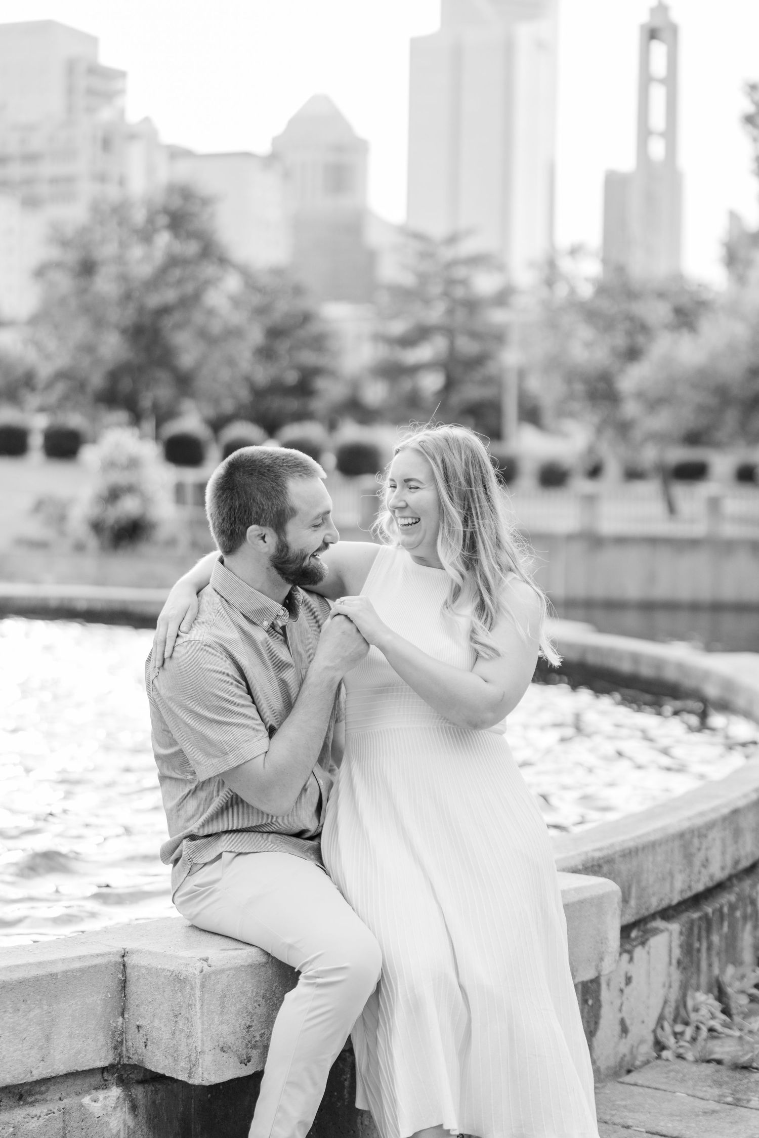 A romantic couple shares a tender moment by a fountain with the city skyline in the background.