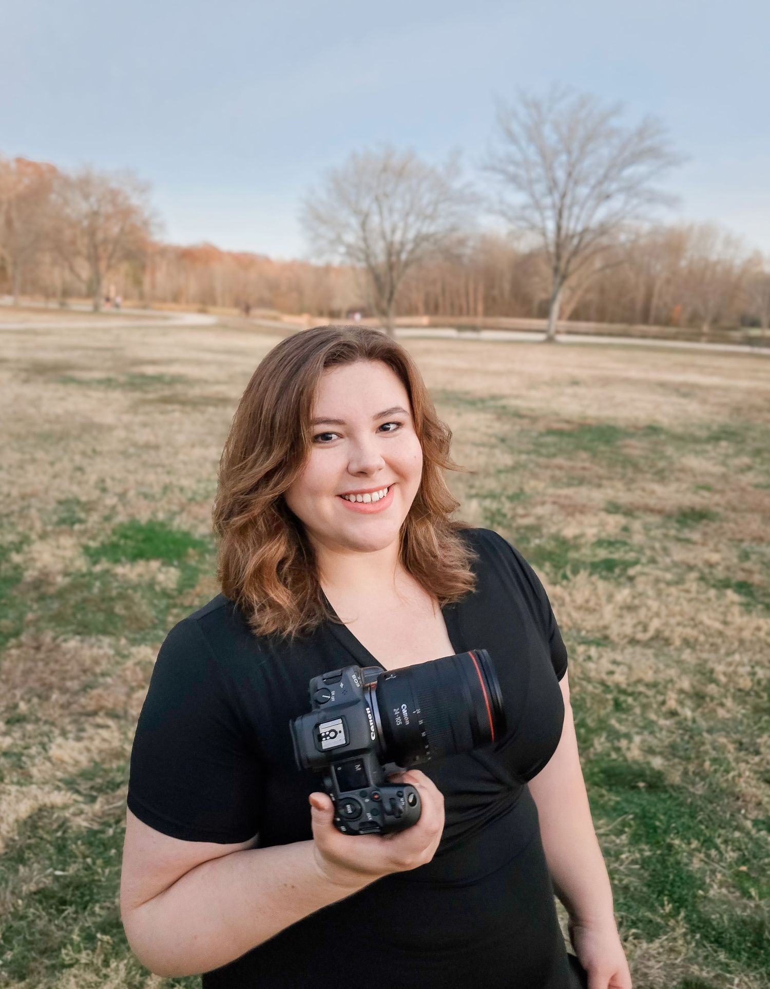 Photographer smiling while holding camera in rural outdoor setting.