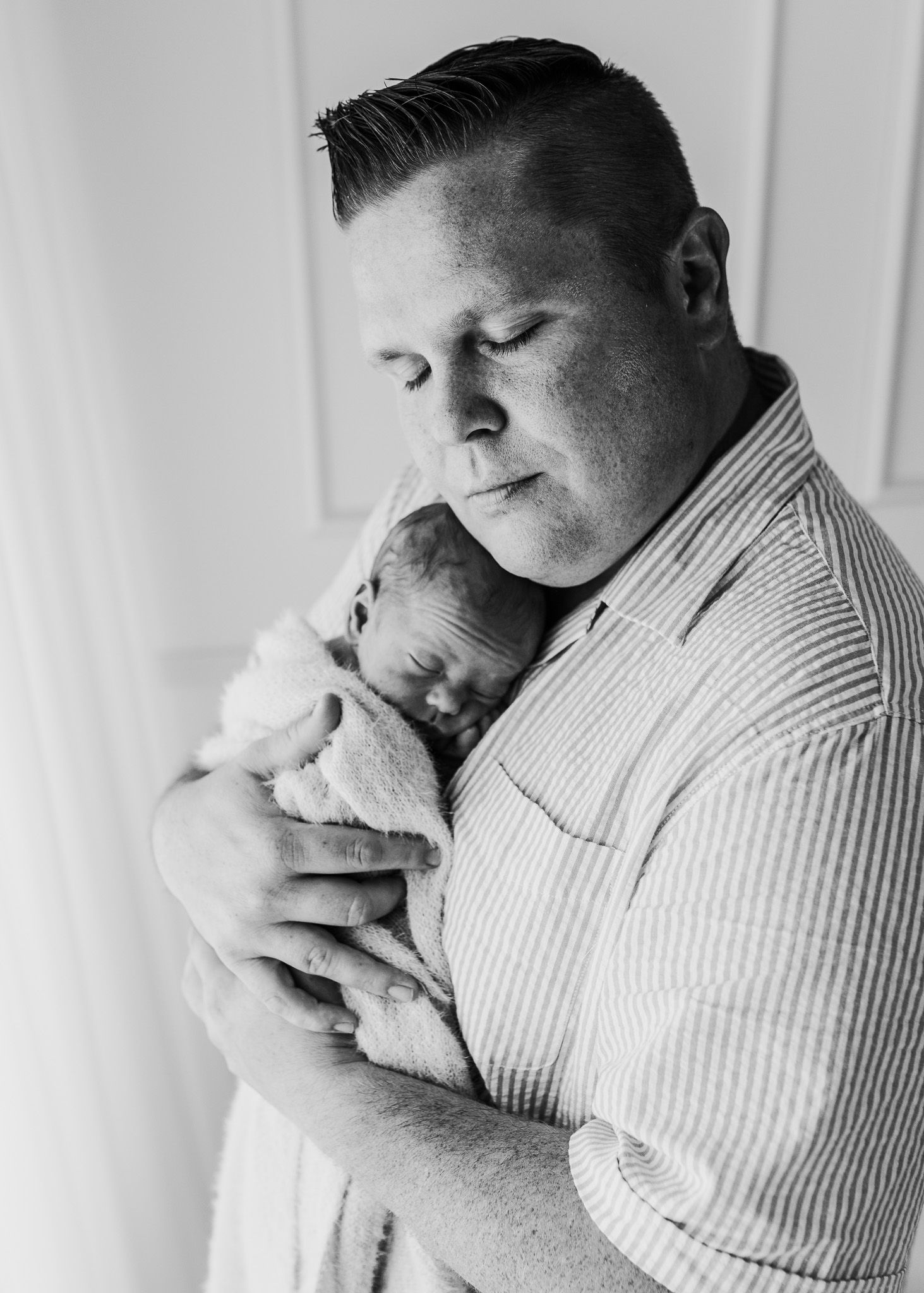A tender black and white portrait of a parent holding a sleeping newborn baby against their chest.