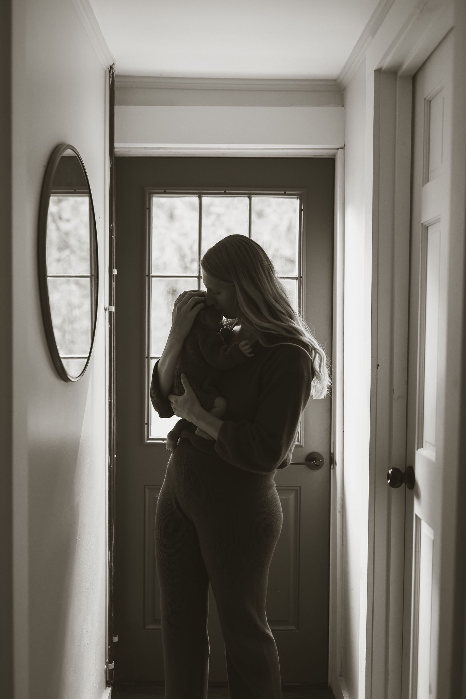 Monochrome portrait of parent cradling baby in front of window with natural light.