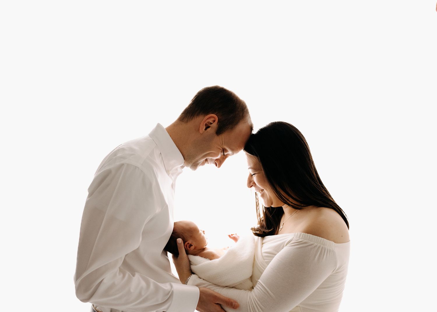 Couple in white clothing embracing during intimate maternity photoshoot.