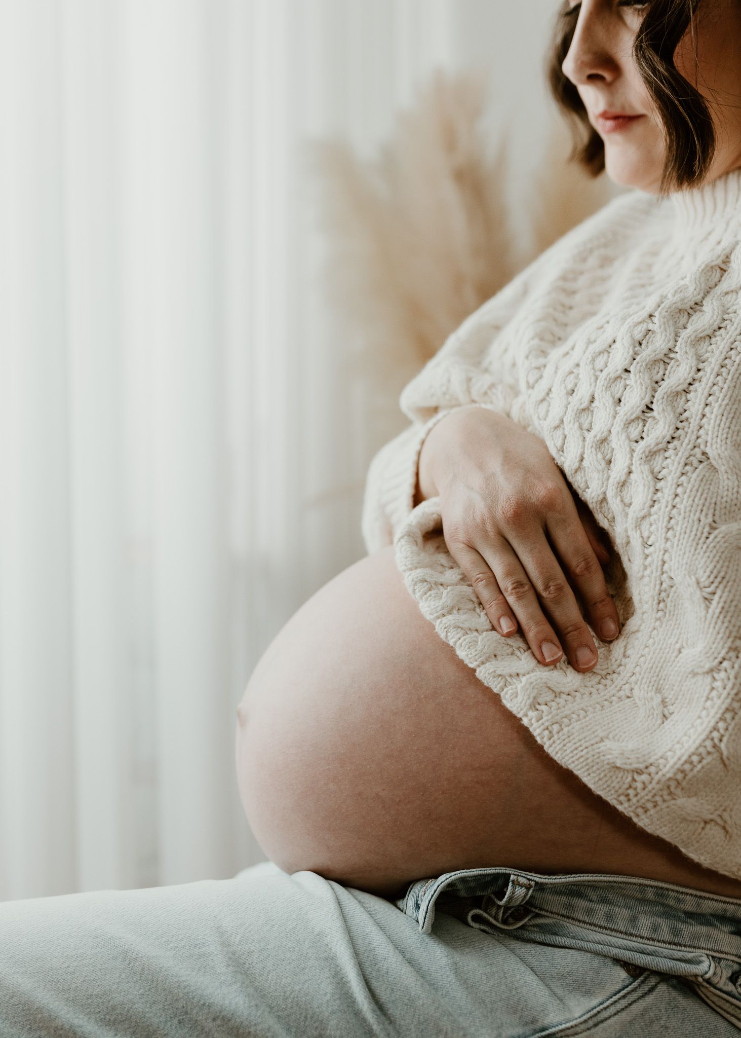 Side view of pregnant woman in white sweater gently holding her baby bump.